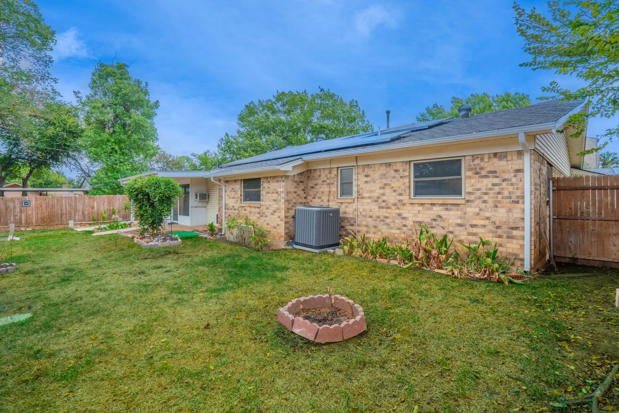 Expansive backyard featuring a manicured lawn, brick exterior, wood privacy fencing, and solar panels