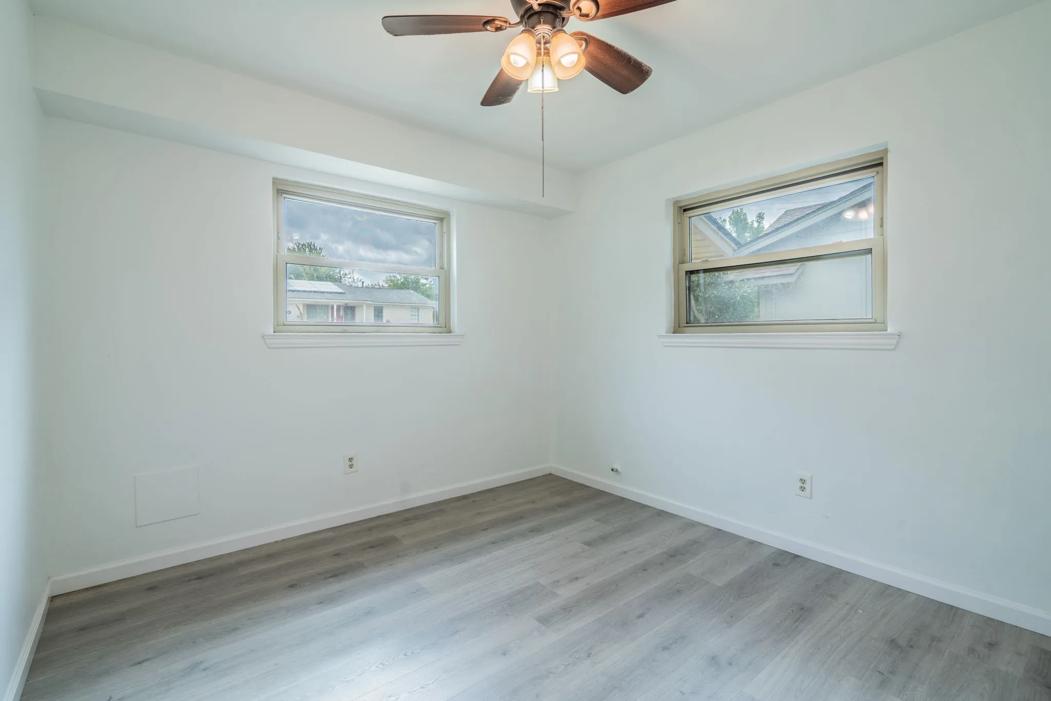 Wood-finish flooring, two windows with trim, and a ceiling fan with integrated lighting