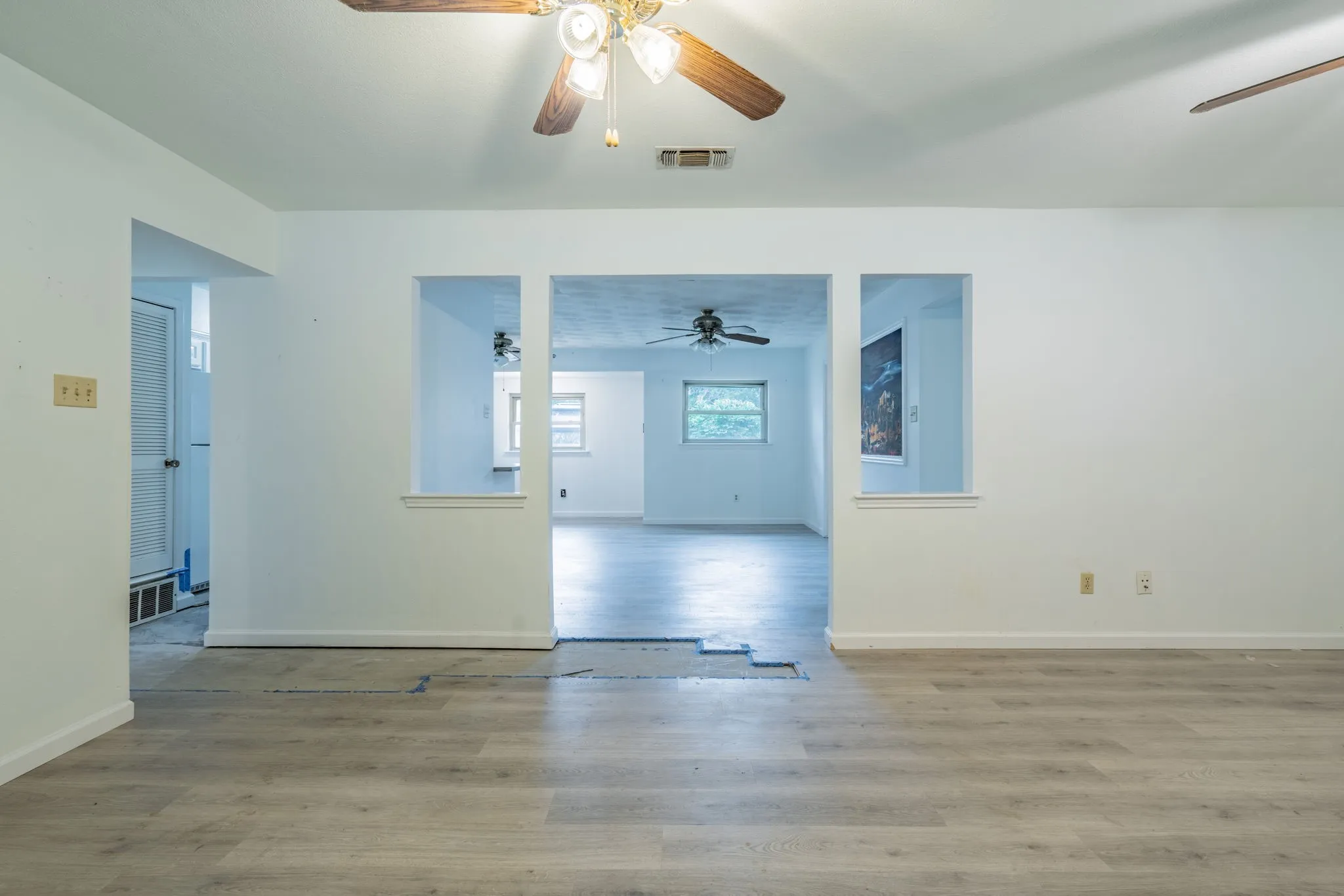 Light wood-finish flooring extending into multiple spaces, featuring white painted walls and ceiling fans