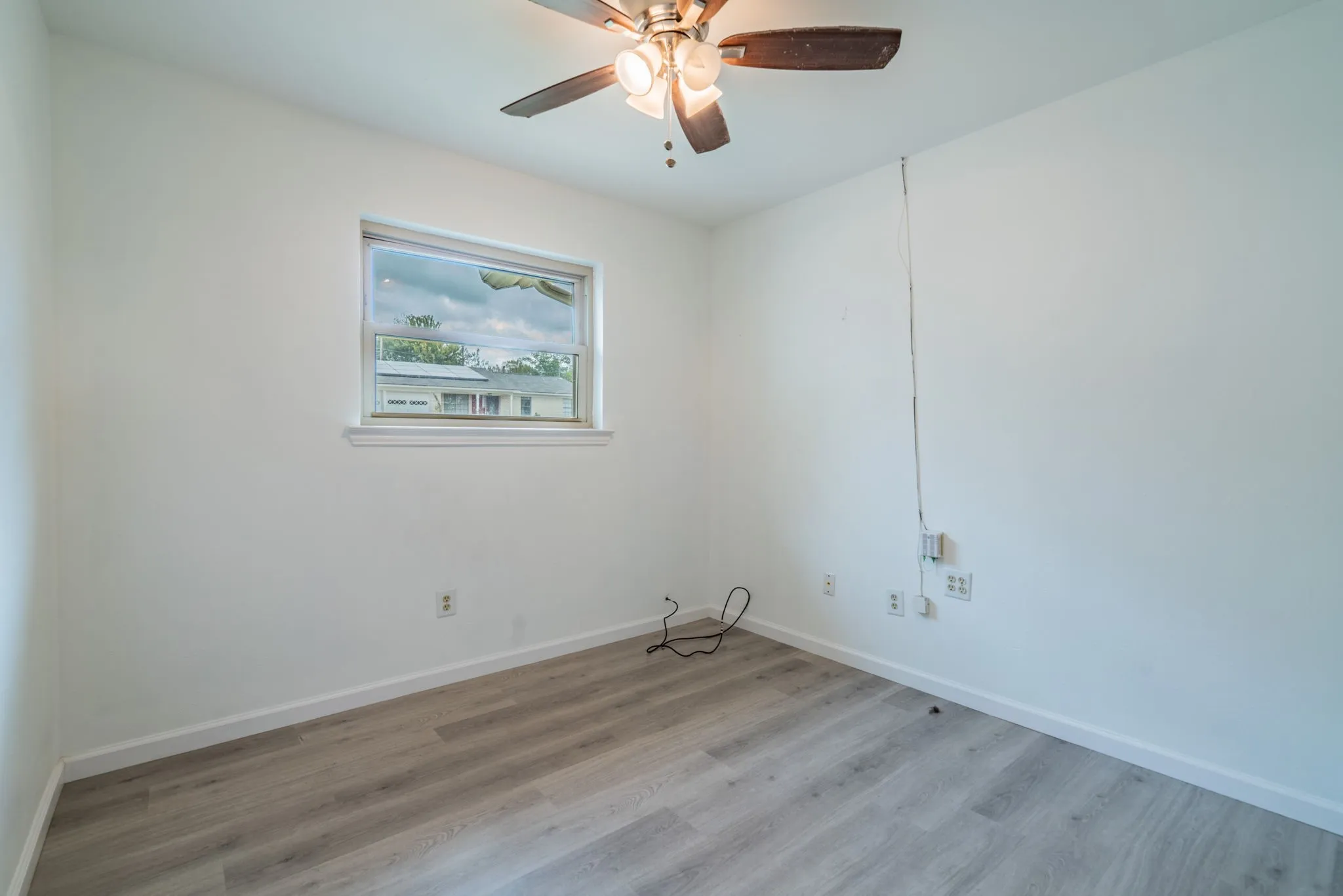 Wood-finish flooring, ceiling fan with integrated lighting, and a single window offering exterior views