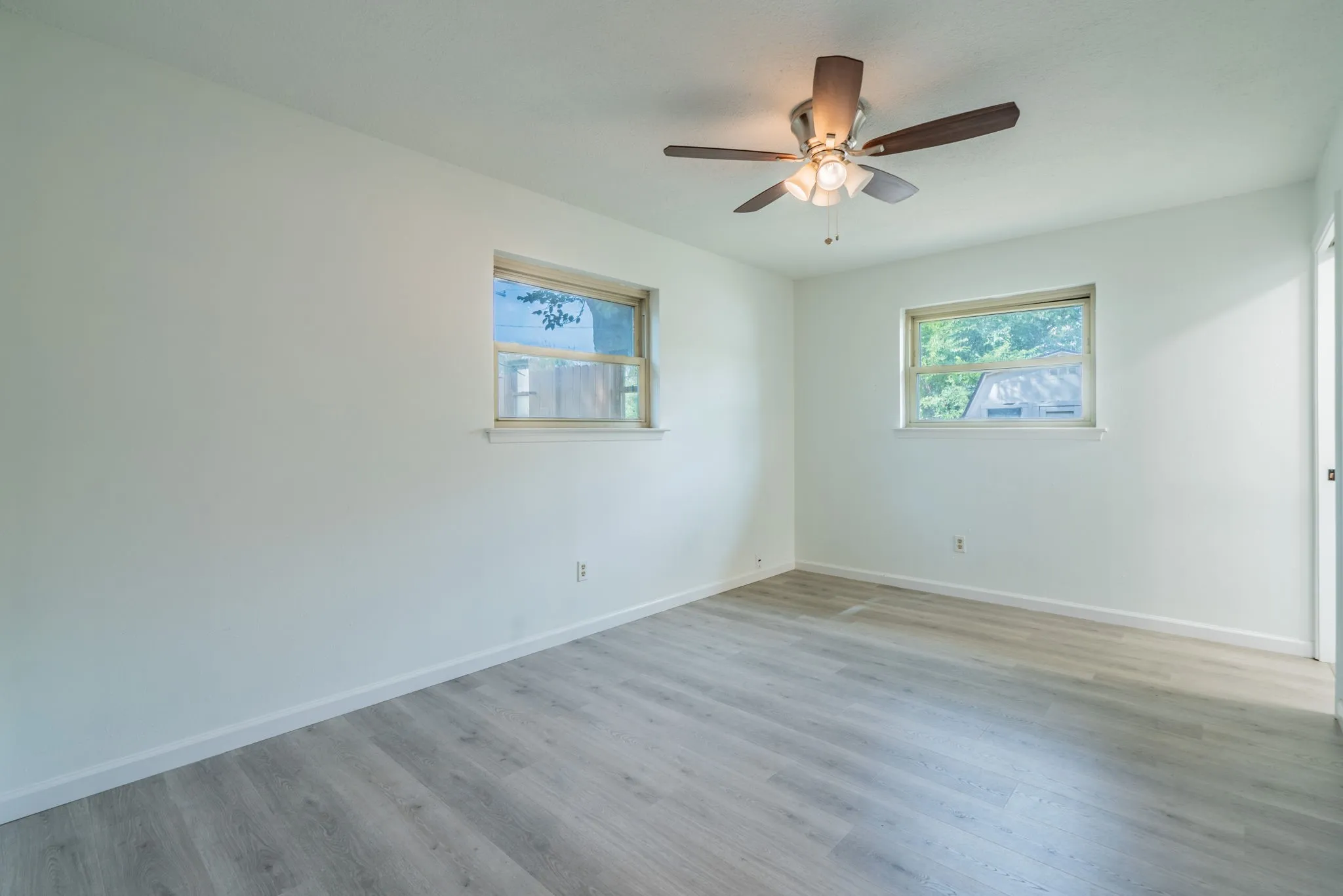 Neutral wall color, wood-finish flooring, two windows, ceiling fan with integrated lighting, white trim