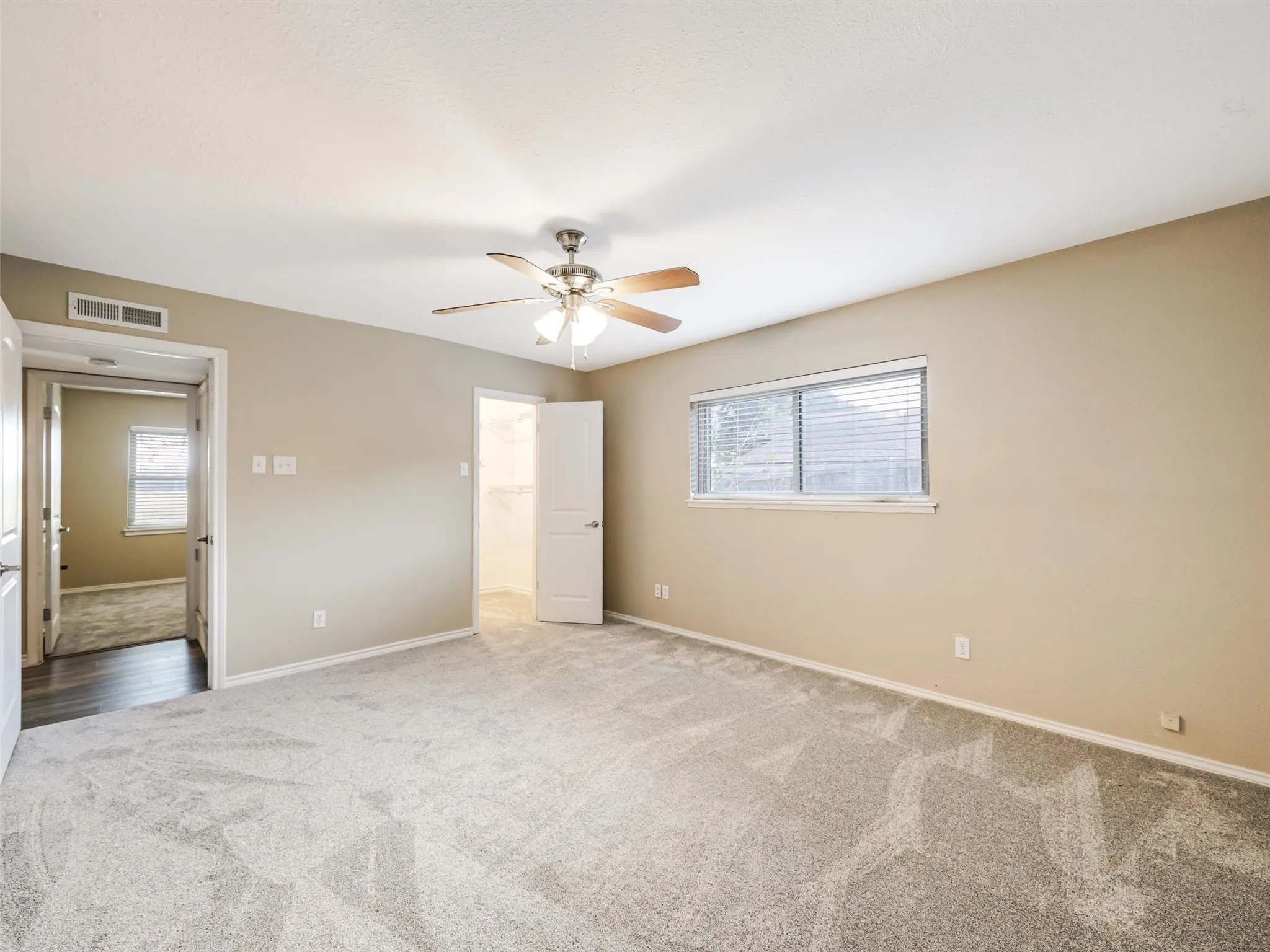 Recessed window with horizontal blinds, ceiling fan with integrated lighting, neutral wall paint, and gray patterned carpeting