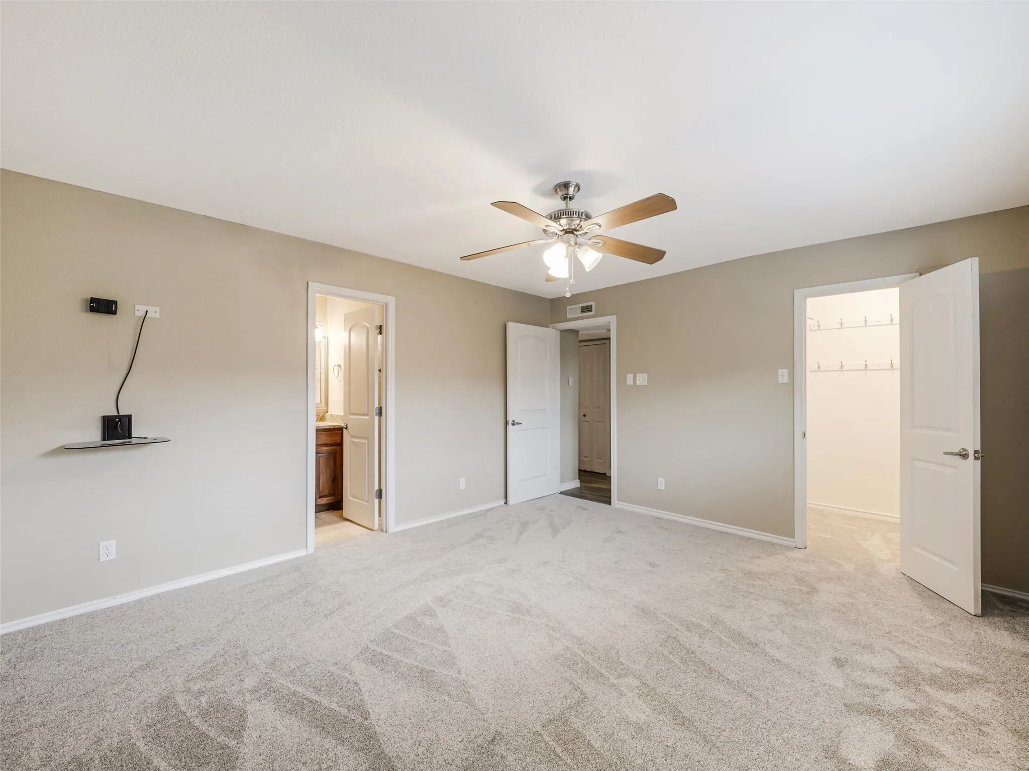 Spacious room with light neutral wall tones, gray patterned carpet, ceiling fan with integrated lighting, and multiple white panel doors