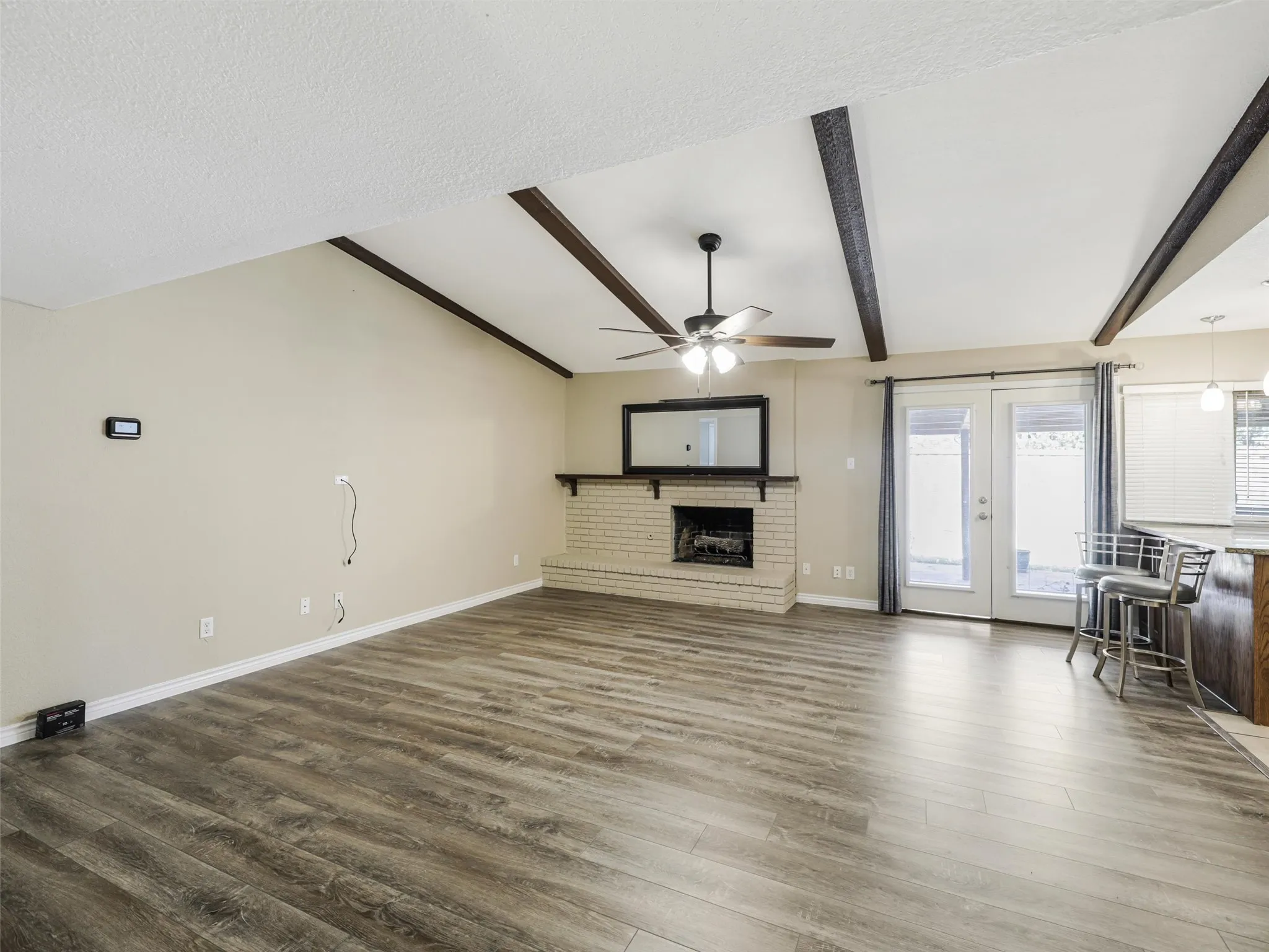 Vaulted ceiling with exposed beams, brick fireplace with mantel, wood-finish flooring, and double glass panel doors