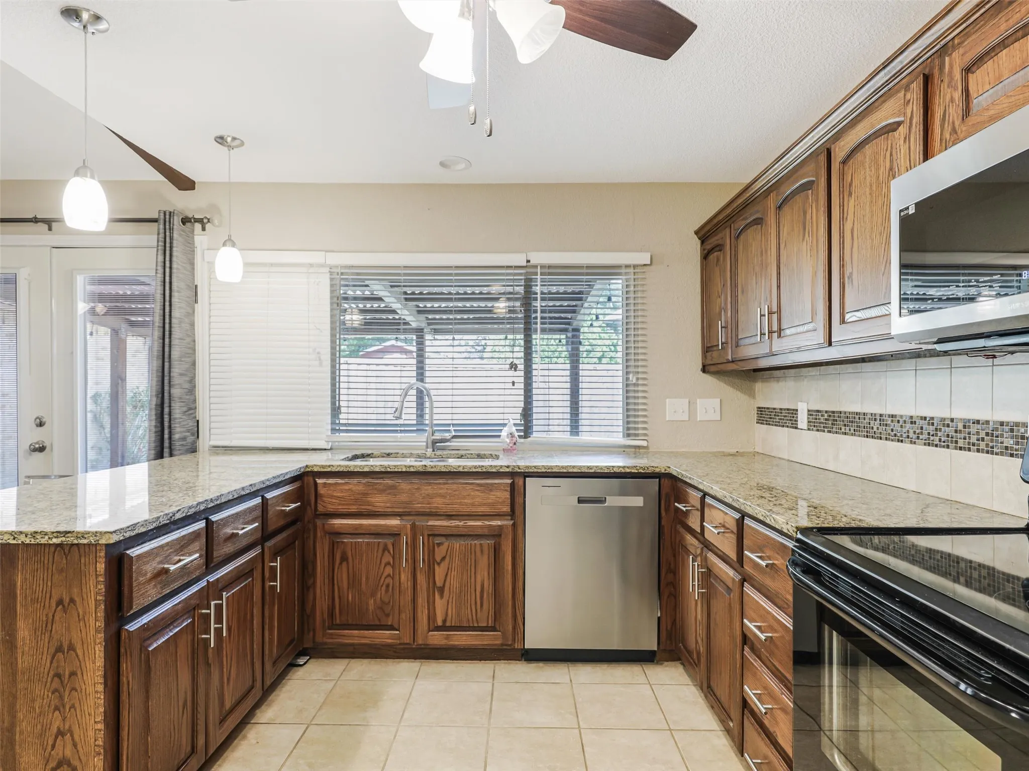 Kitchen featuring wood cabinetry, granite countertops, tile flooring, stainless steel dishwasher, and pendant lighting