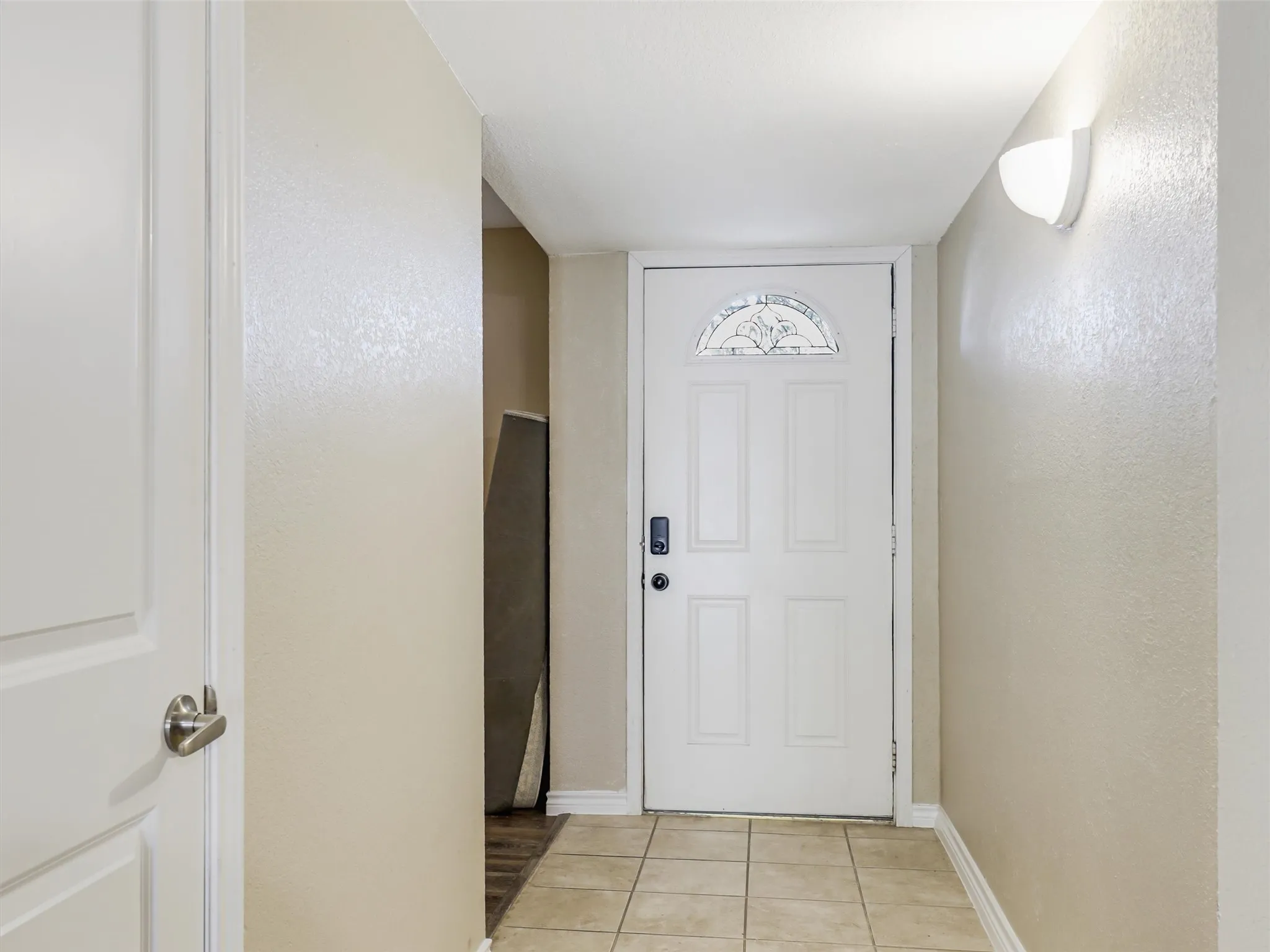 Front entry with a decorative glass door, tiled flooring, and a wall-mounted light fixture