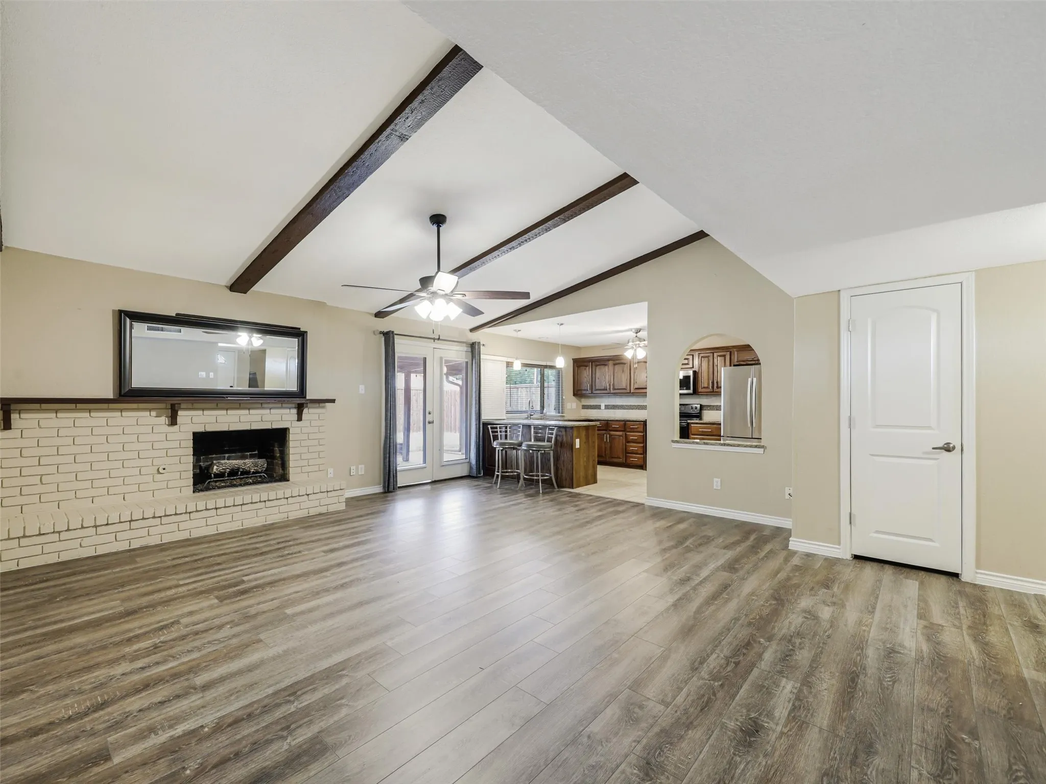 Vaulted ceiling with exposed wood beams, brick fireplace, wood-finish flooring, and French doors