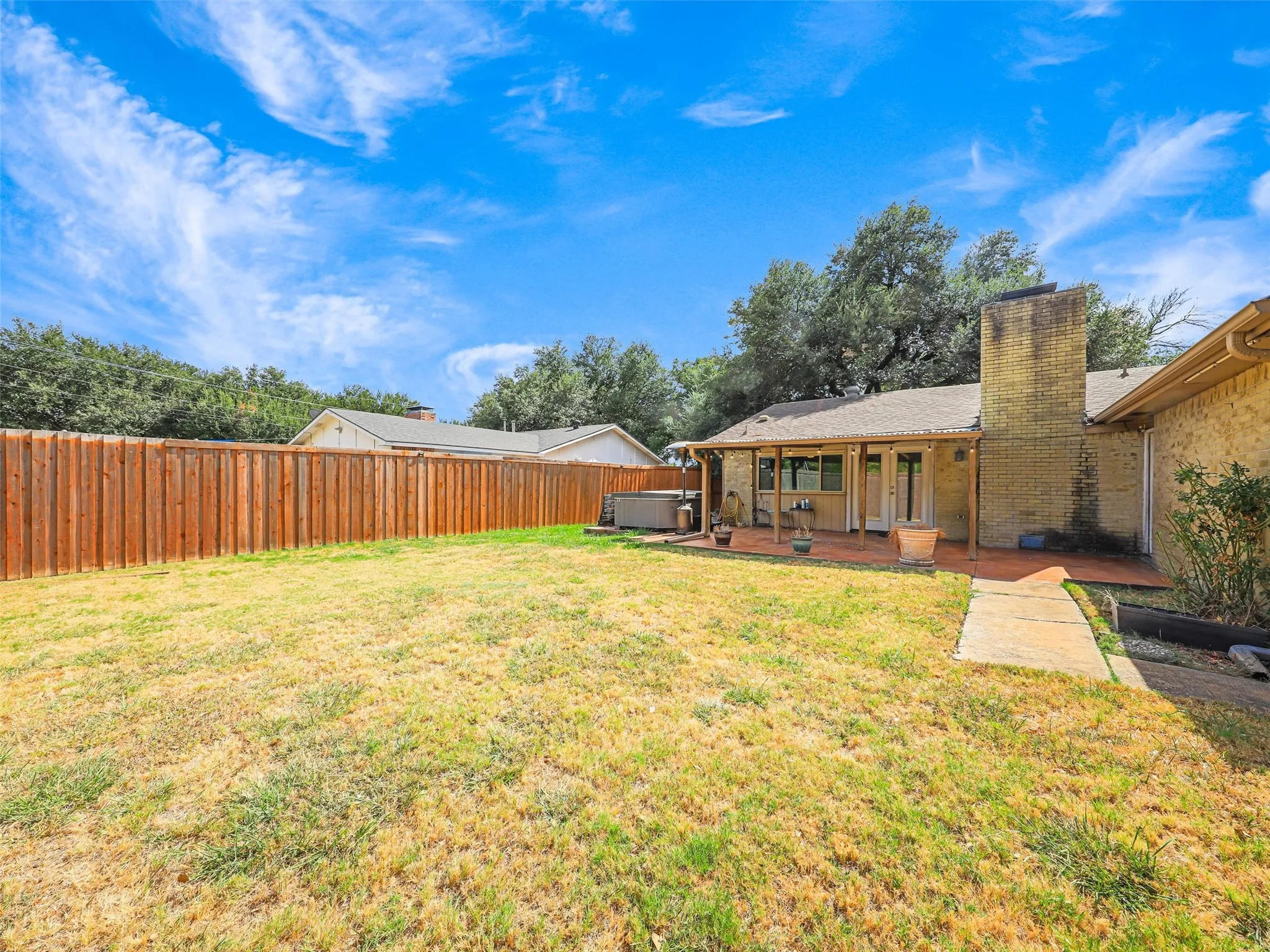 Expansive backyard with a full privacy fence, covered patio, and brick exterior
