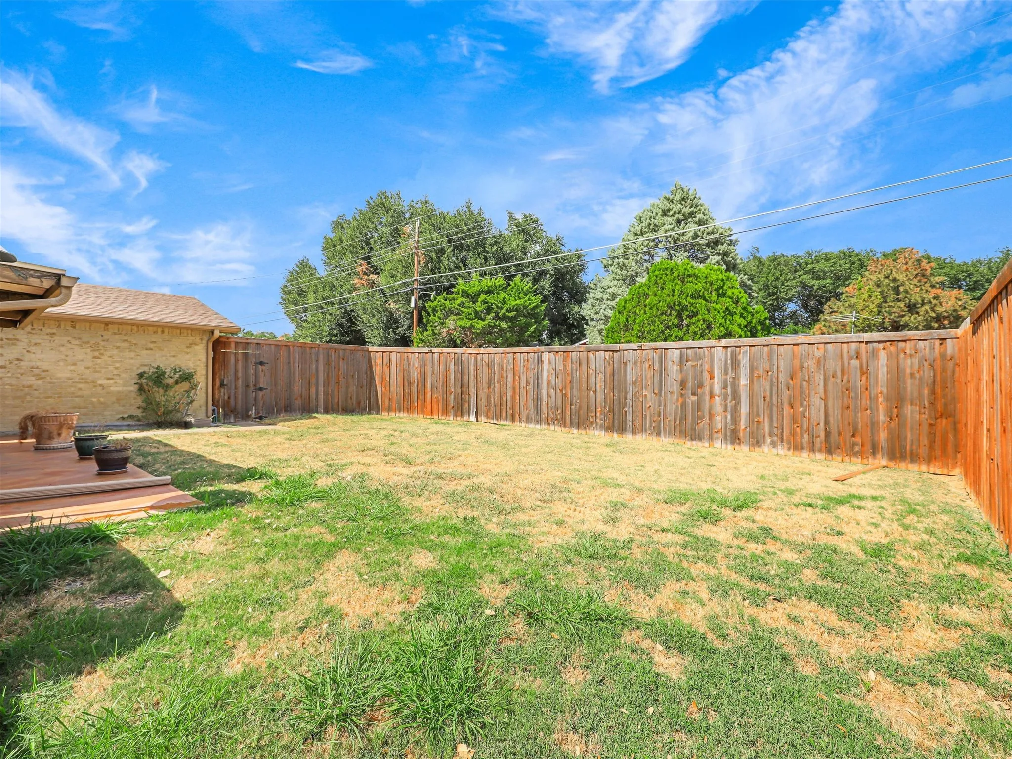 Spacious backyard featuring a wood deck, wood privacy fencing, and mature perimeter trees