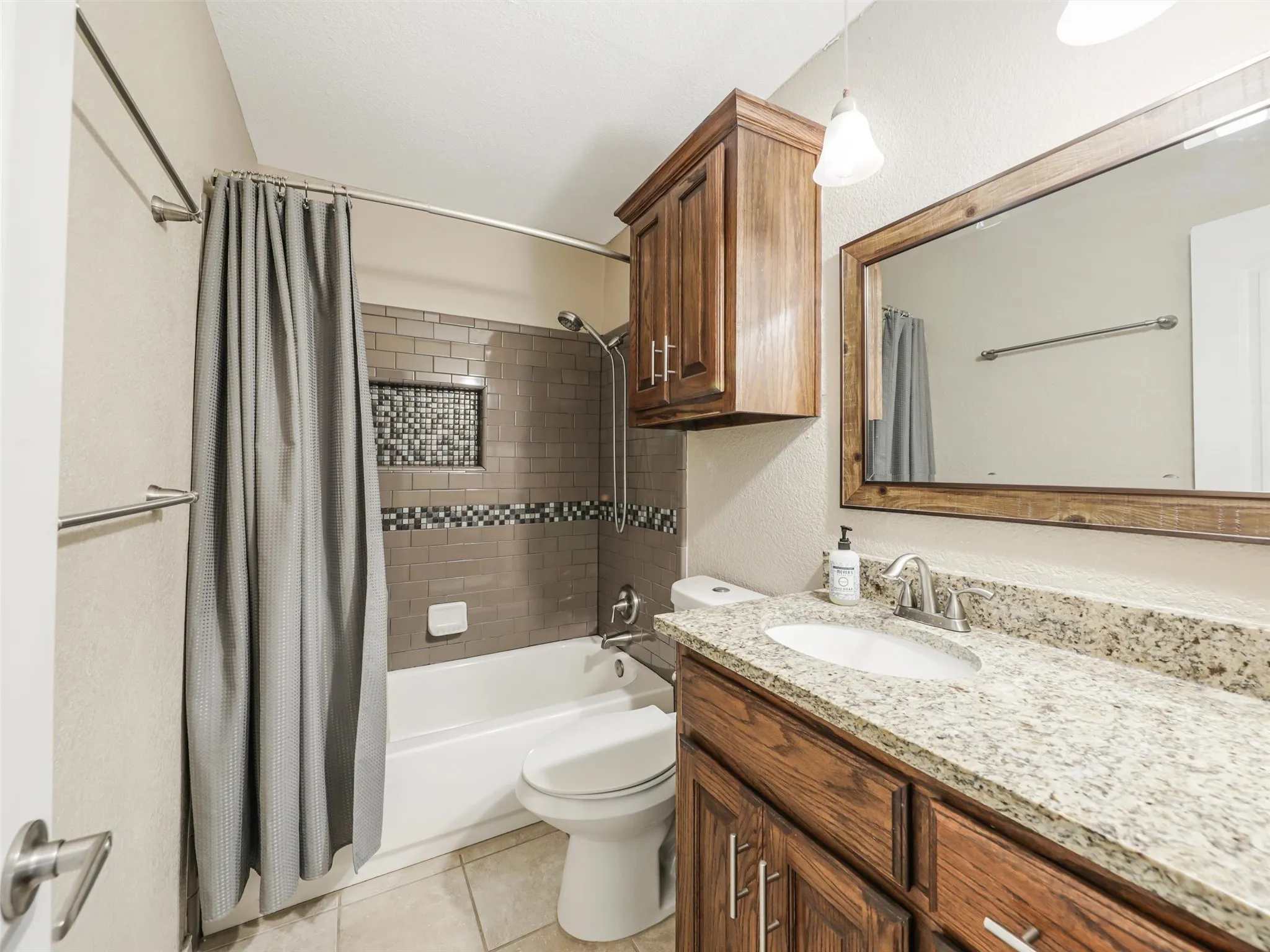 Bathroom featuring a granite-style countertop, wood-finish vanity, framed mirror, and tiled shower surround with an inset niche