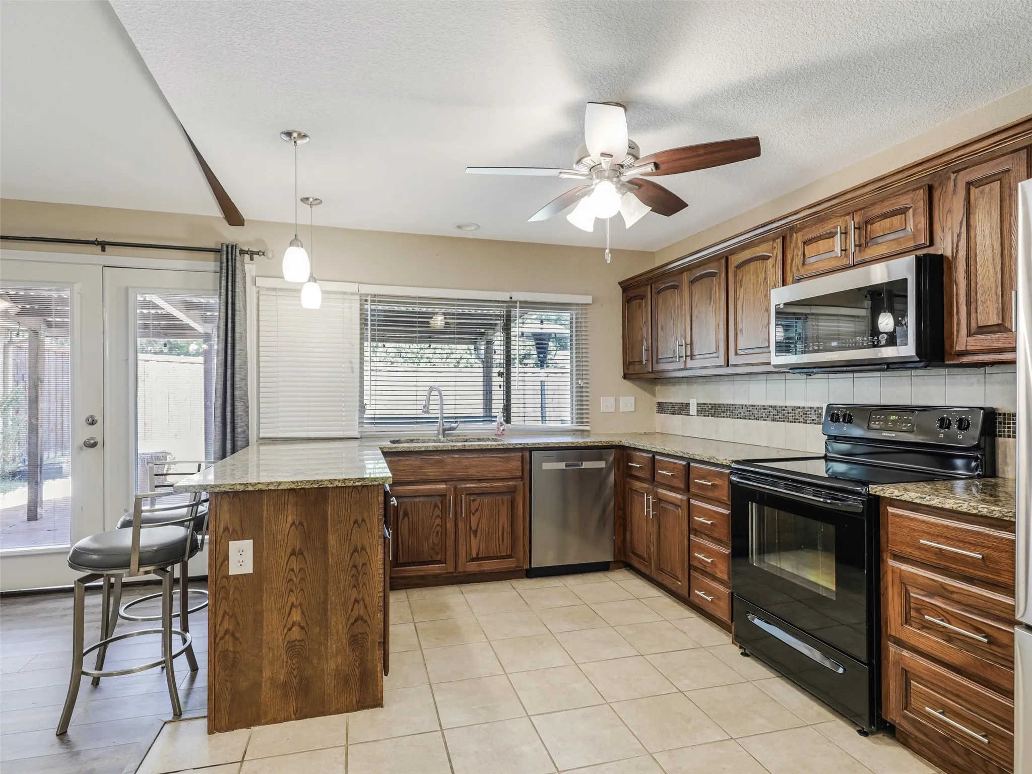 Well-appointed kitchen featuring wood cabinetry, light-toned tile flooring, and integrated stainless steel appliances