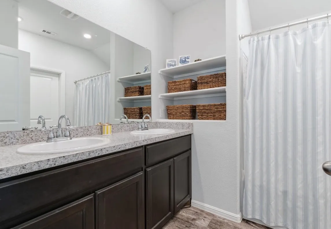 Dual undermount sinks set into a granite-finish countertop, dark wood-finish cabinetry, and an expansive vanity mirror
