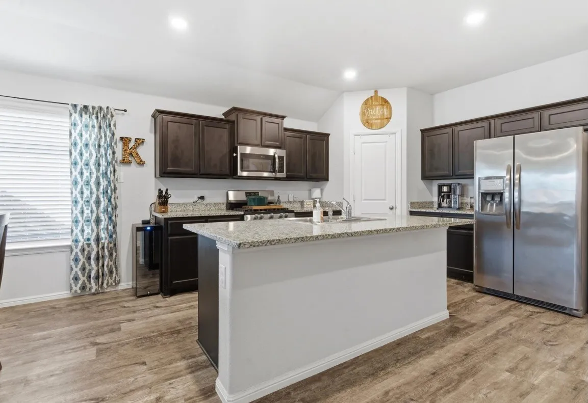 Spacious kitchen featuring wood-finish flooring, dark wood cabinetry, light-colored countertops, a kitchen island, and stainless steel appliances