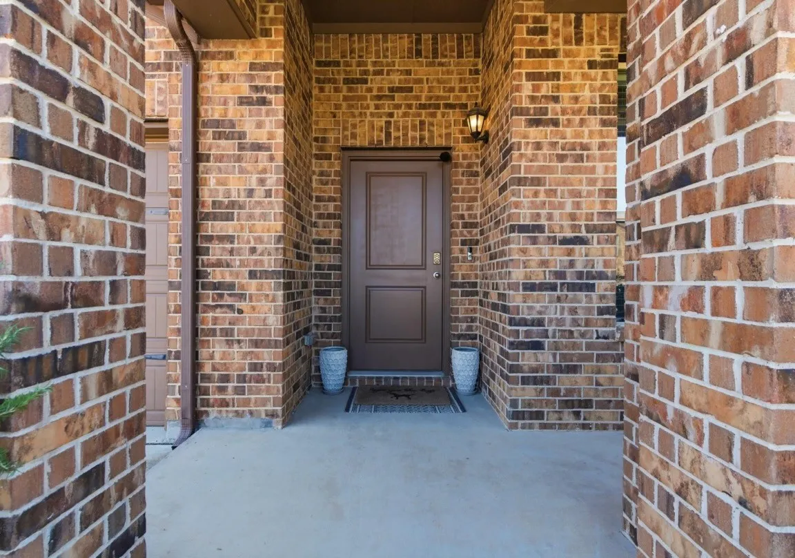 Brick exterior with a covered entry, concrete porch, and an exterior wall lantern
