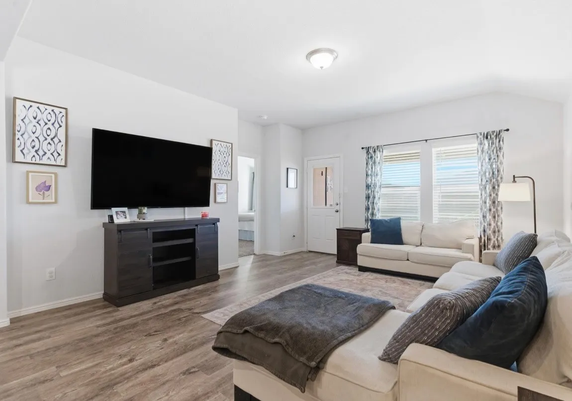 Spacious living area featuring wood-finish flooring, a contemporary media console, and a ceiling-mounted light fixture
