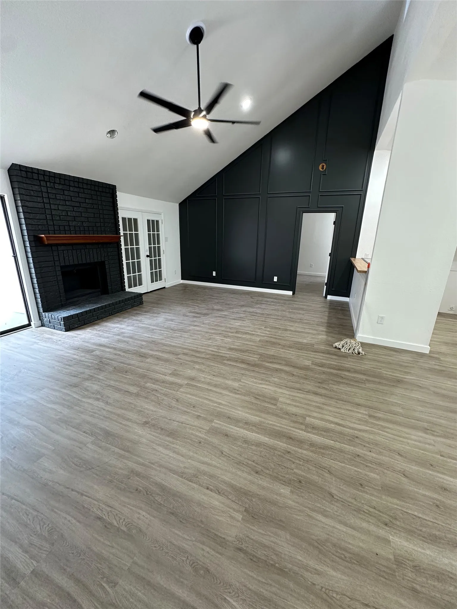 Vaulted ceiling with contemporary ceiling fan, dark brick fireplace with wood mantel, wood-finish flooring, and French doors