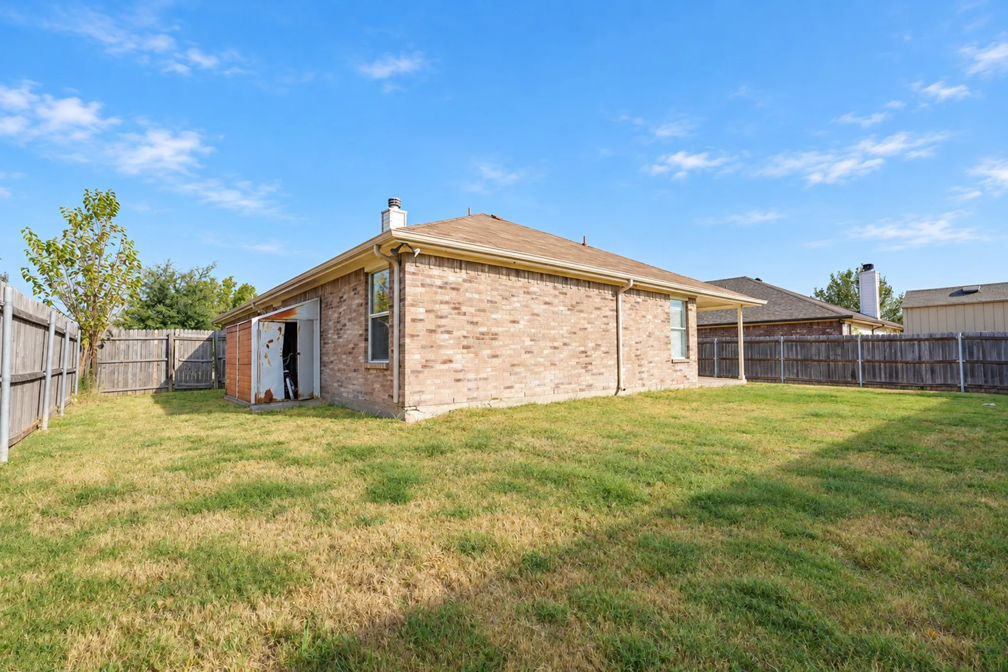 Fenced backyard featuring a brick exterior, shingle roof, and a covered patio area
