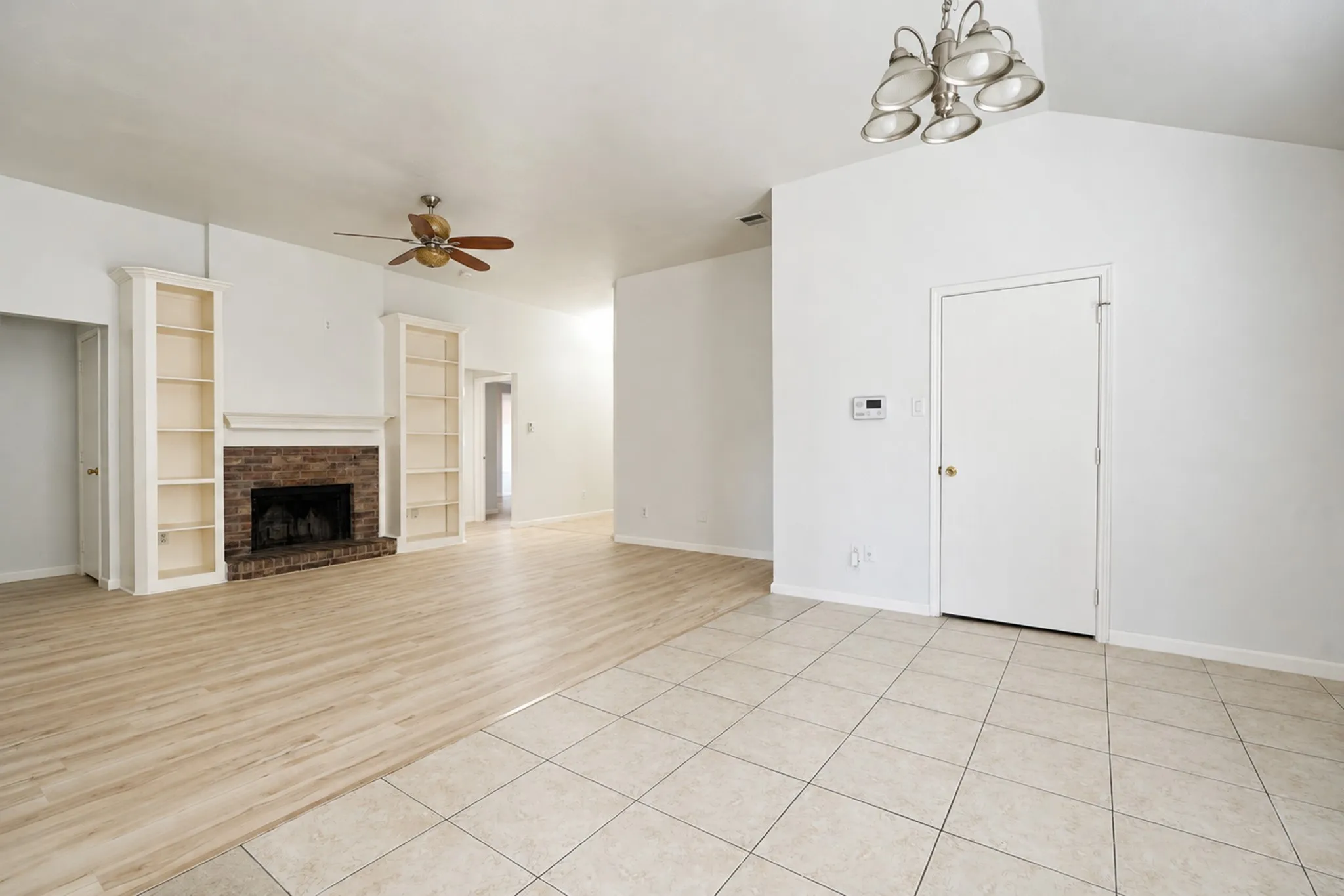 Vaulted ceiling with an attached light fixture, wood-finish flooring, tiled flooring, brick fireplace, and built-in shelving