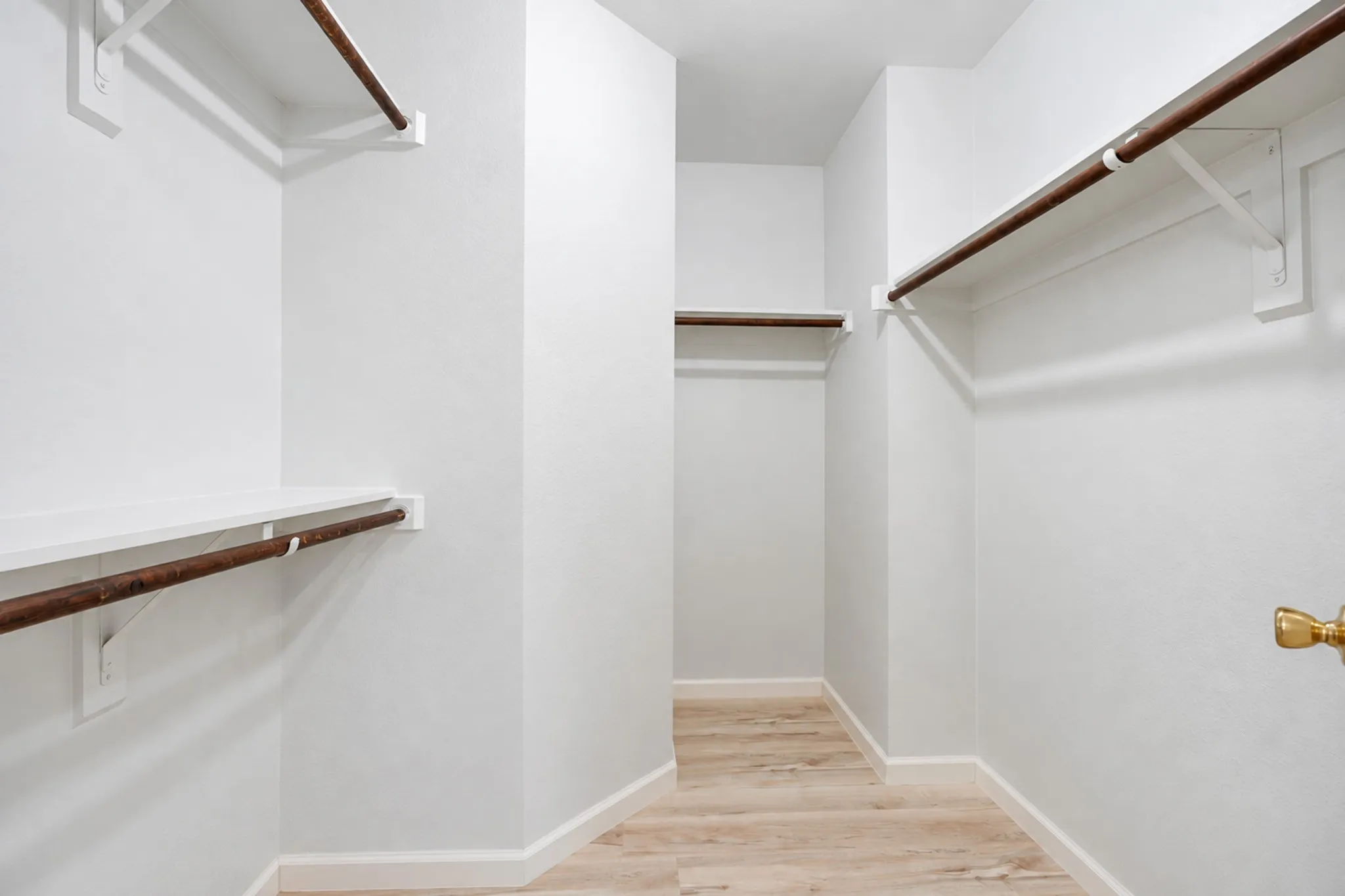 Walk-in closet with multiple hanging rods, integrated shelving, white walls, and wood-finish flooring