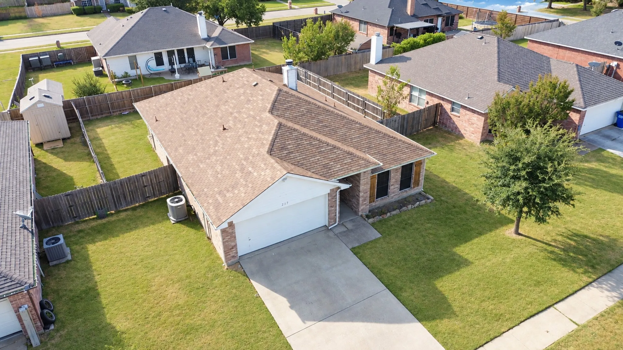 Brick facade residence with an attached two-car garage, mature landscaping, and a fenced backyard