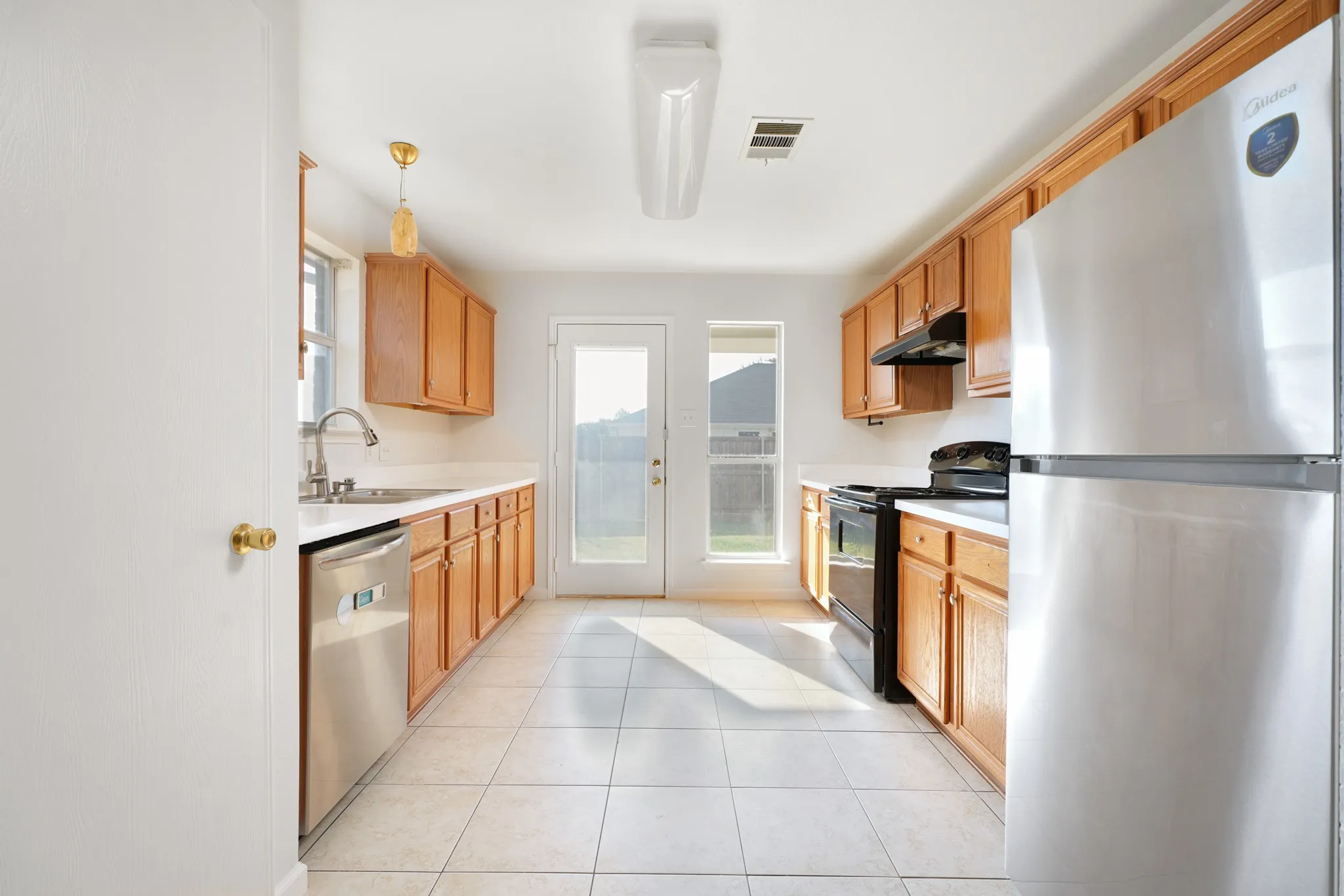 Galley kitchen featuring wood-finish cabinetry, white countertops, tile flooring, stainless steel refrigerator, and a glass-paneled exterior door