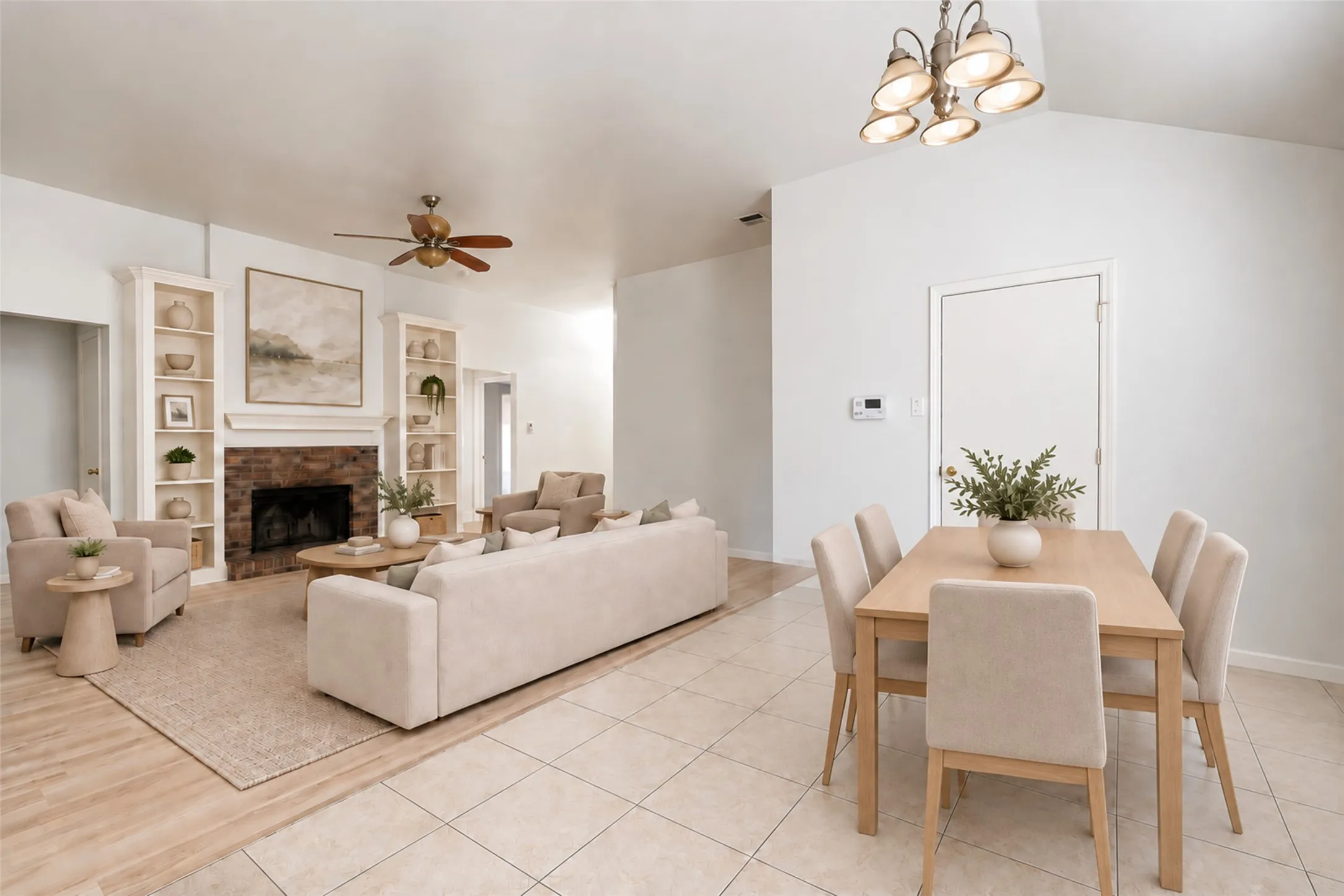 Vaulted ceiling with an attached light fixture, a brick fireplace, built-in shelving, a ceiling fan, and tile flooring