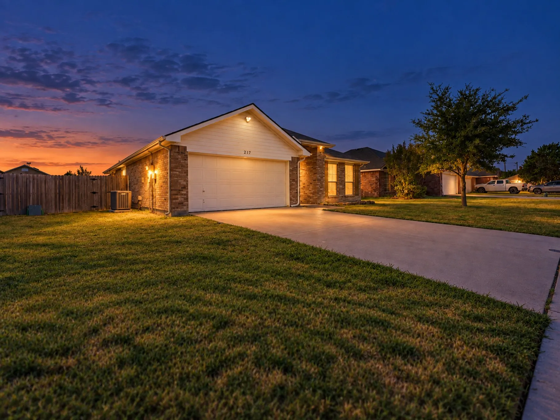Brick and siding exterior with an attached garage, concrete driveway, and a wood privacy fence