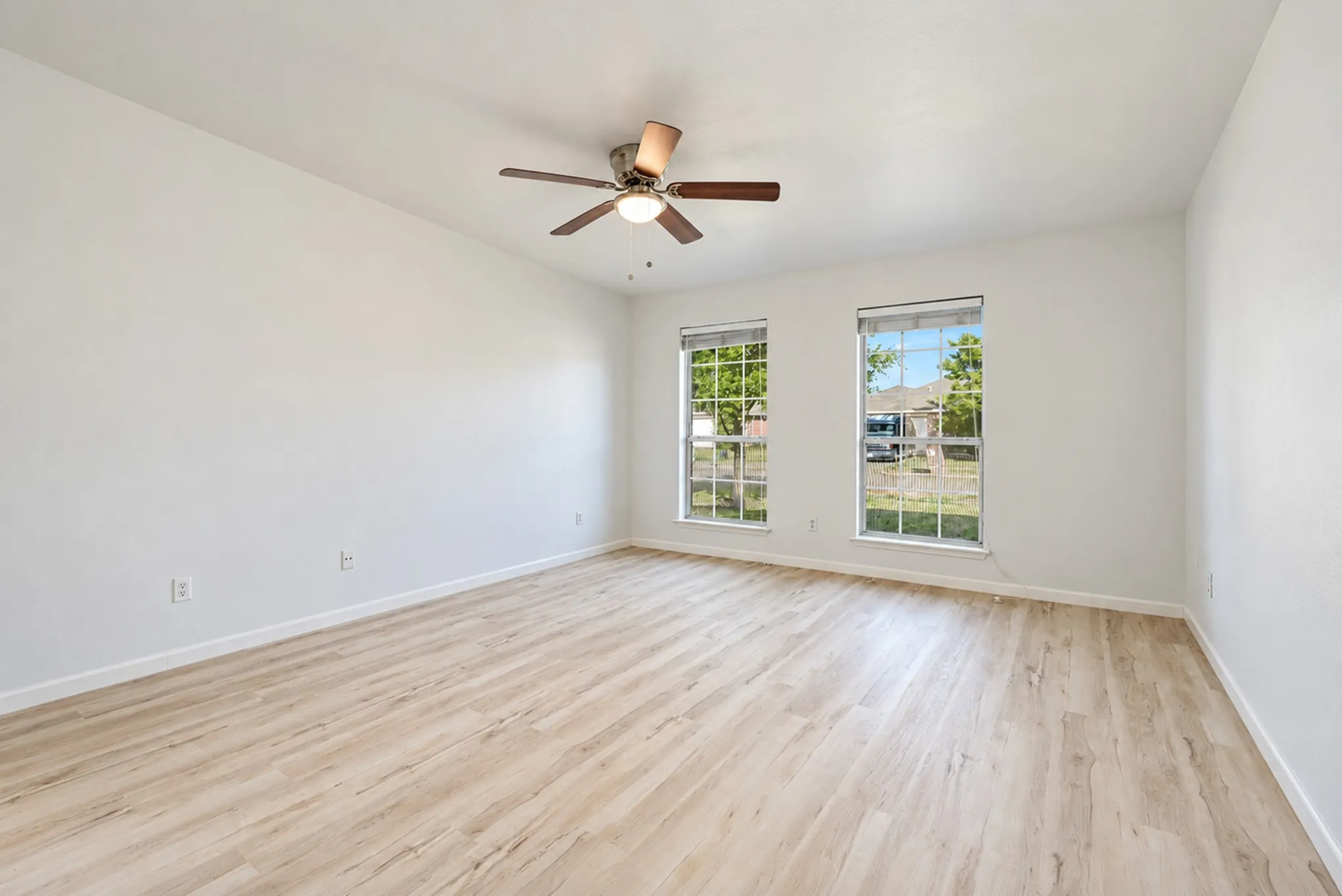 Spacious room featuring wood-finish flooring, two windows, and a ceiling fan with integrated lighting
