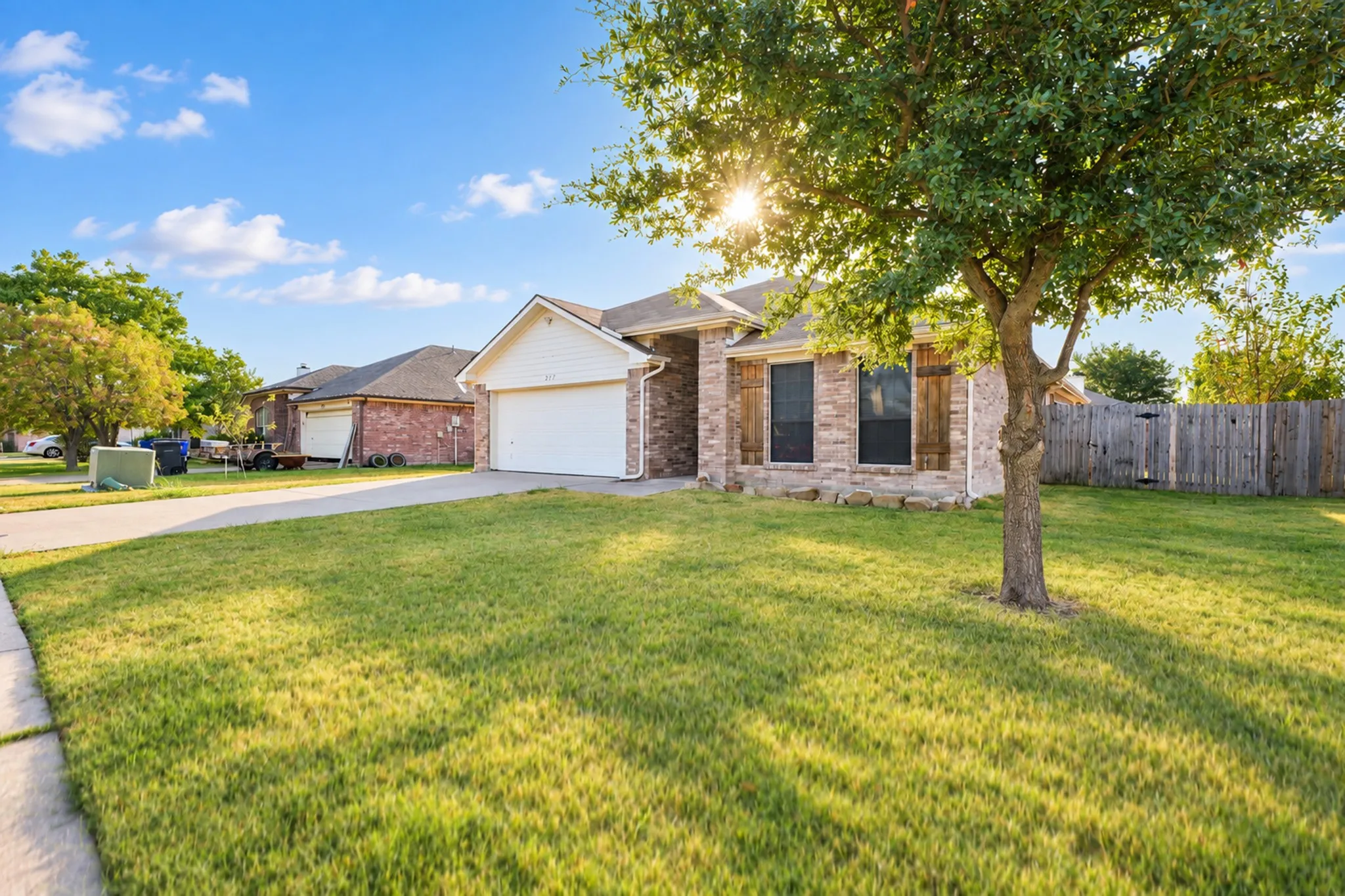 Brick and stone exterior, attached garage, front lawn, mature tree, wood fencing