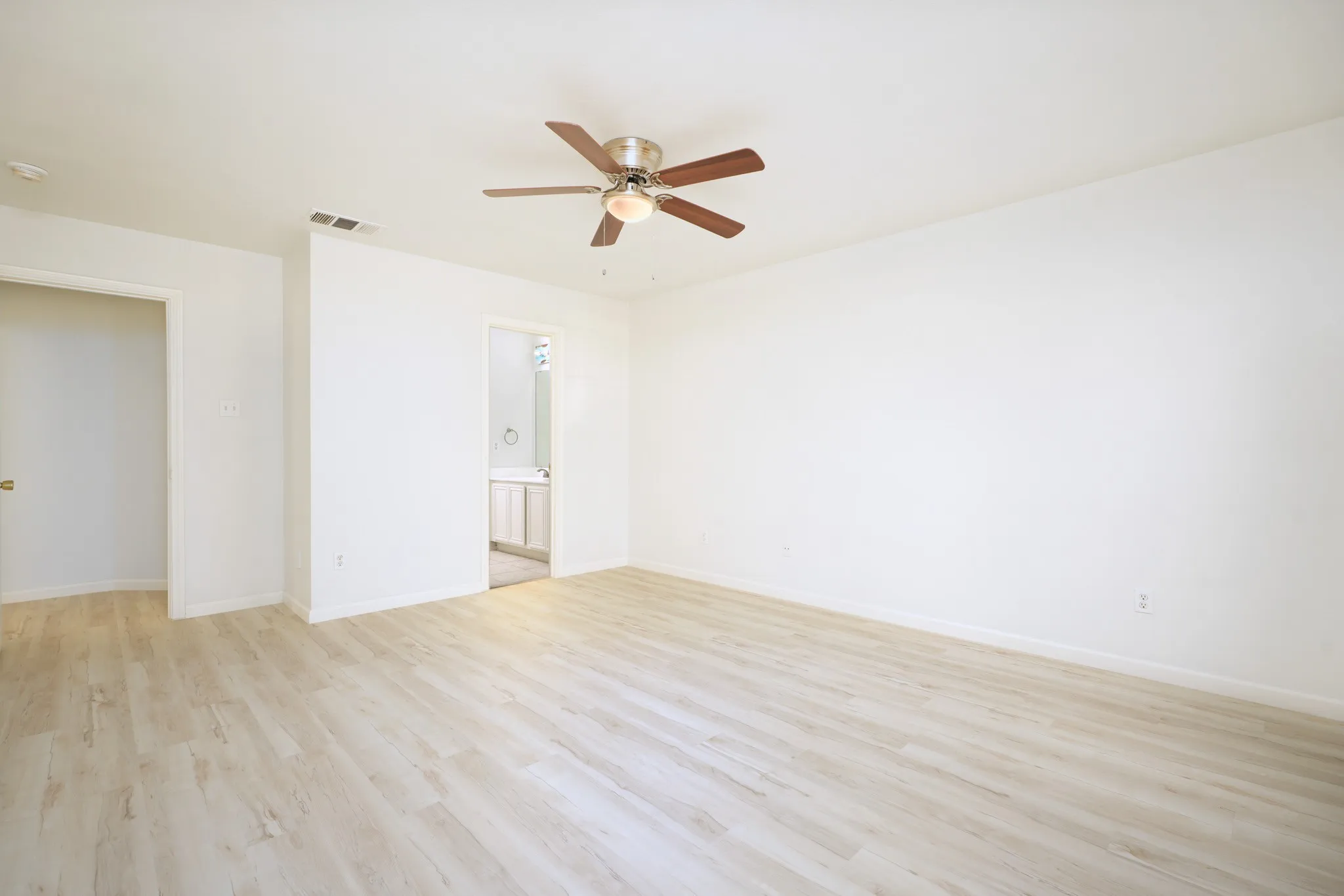 Wood-finish flooring, ceiling fan with integrated lighting, recessed door frame, and white wall finishes