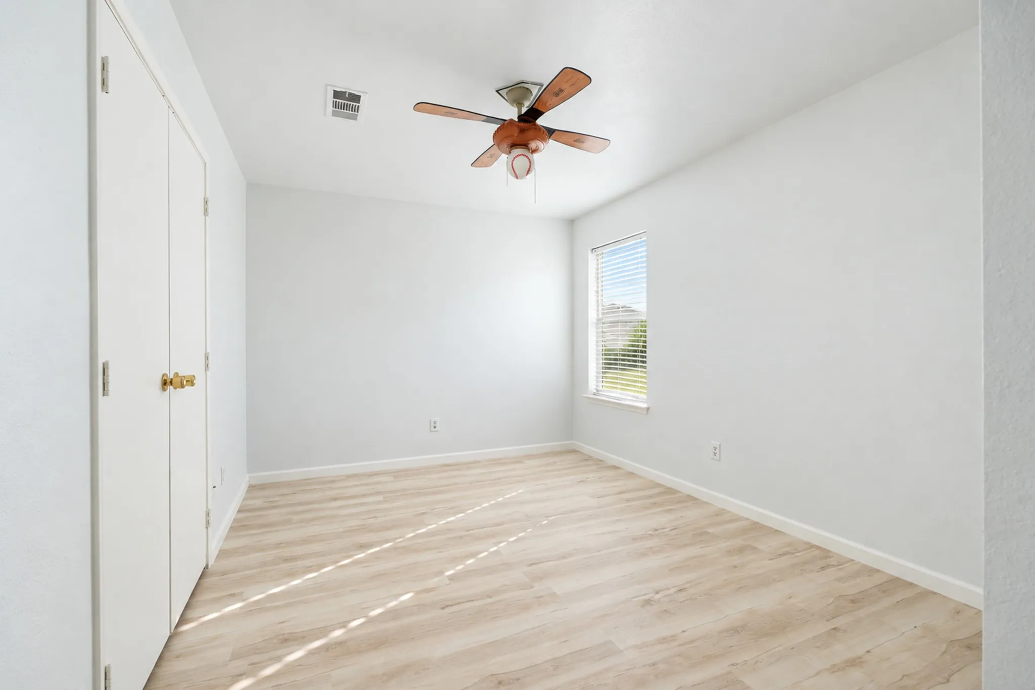 Light wood-finish flooring, a window with horizontal blinds, and a ceiling fan