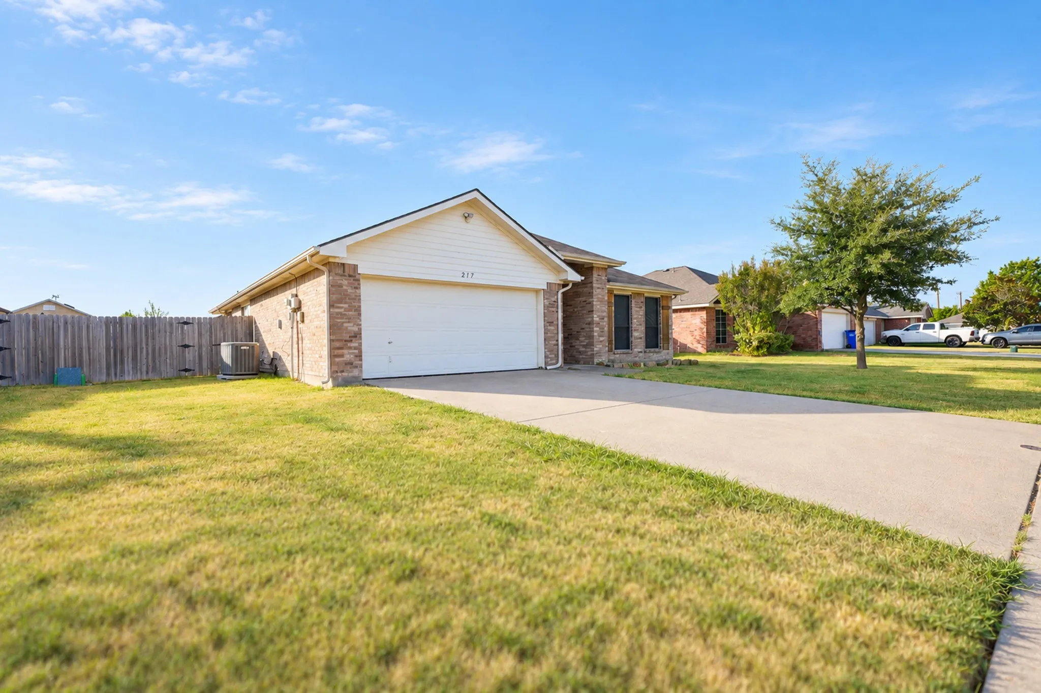 Brick exterior with siding accents, attached two-car garage, concrete driveway, and a fenced side yard