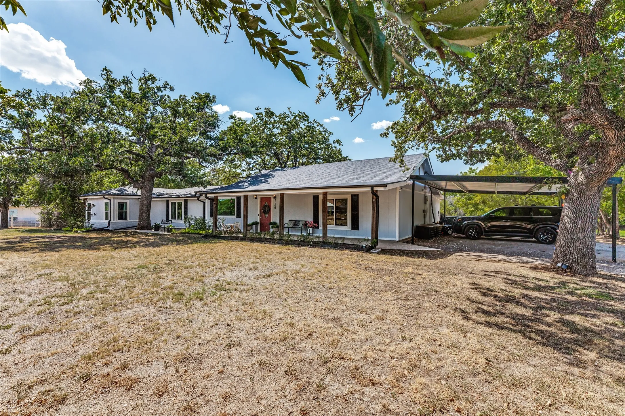 Single-story exterior with a covered porch, white siding, dark shutters, and a covered carport