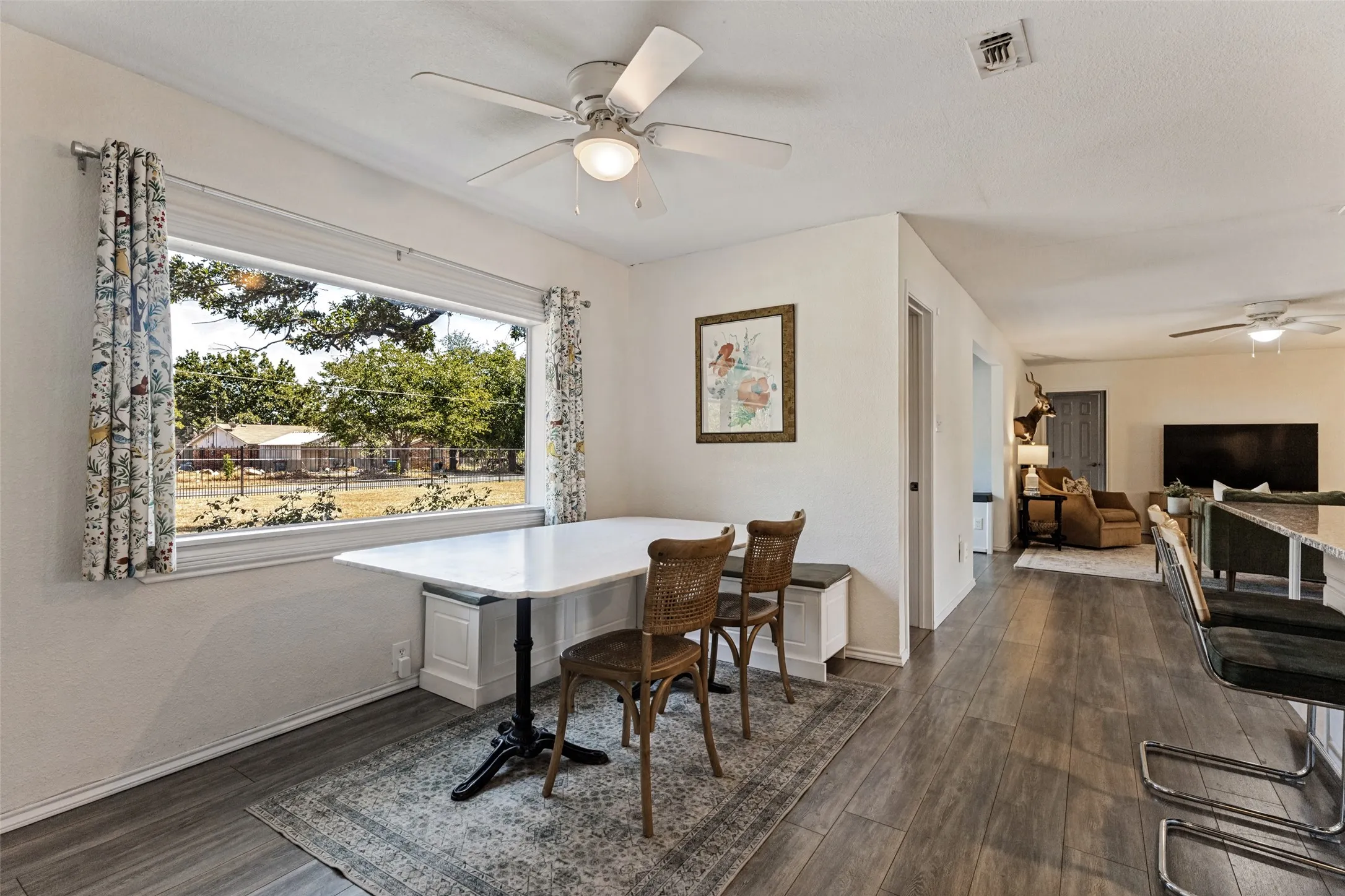 Wide picture window, wood-finish flooring, ceiling fan, white baseboards, recessed lighting