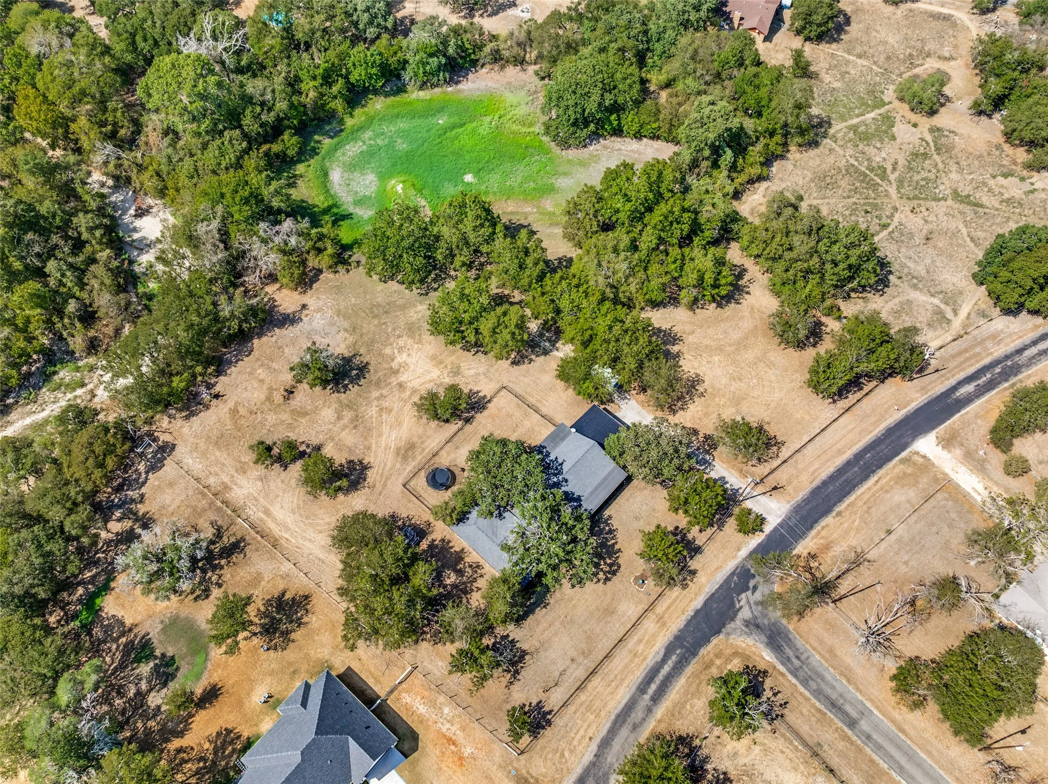 Expansive natural landscape featuring a single-story residence, mature trees, and a paved road network