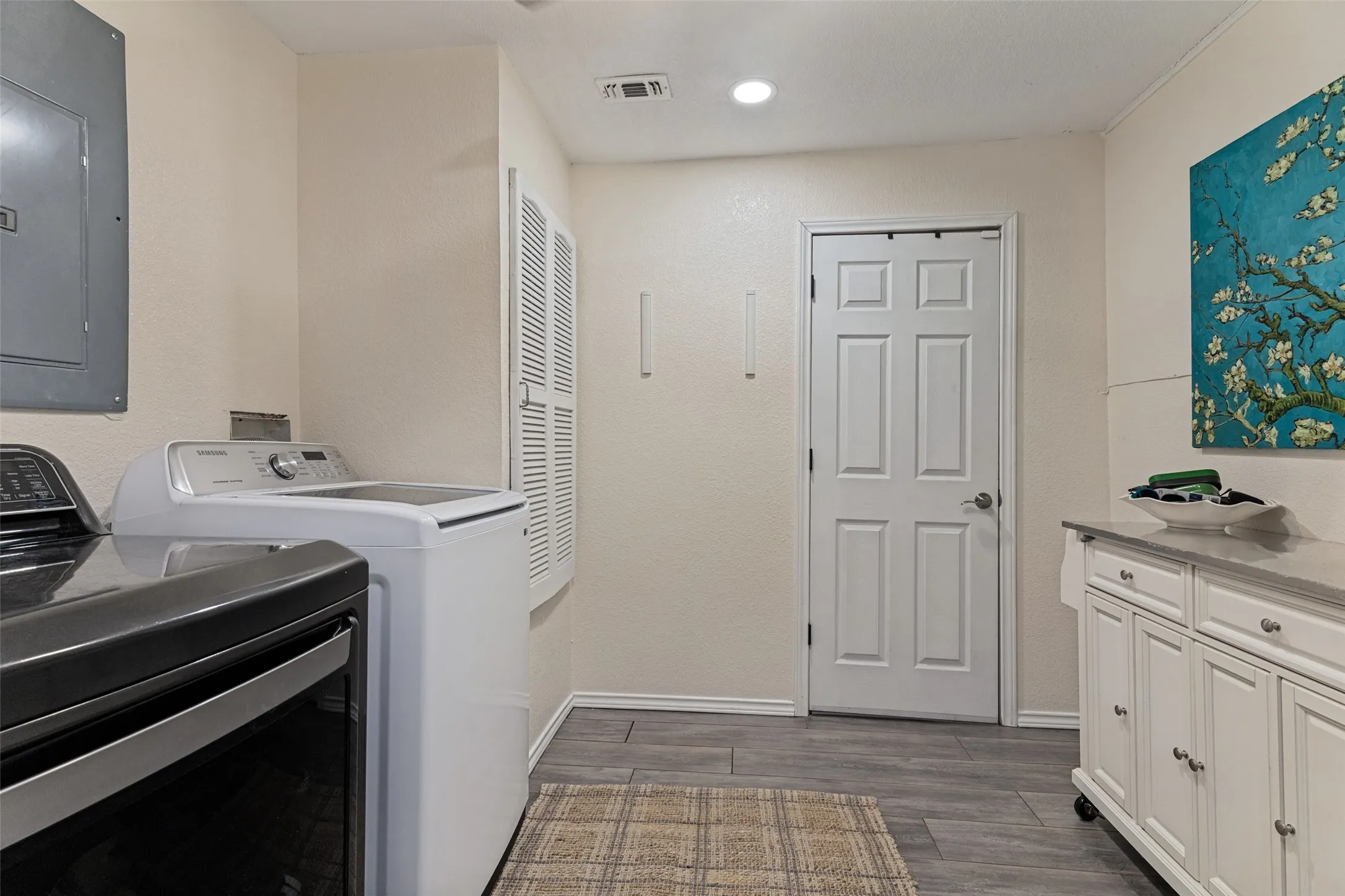 Spacious utility room featuring wood-finish flooring, recessed lighting, built-in cabinetry with a countertop, and a louvered door closet