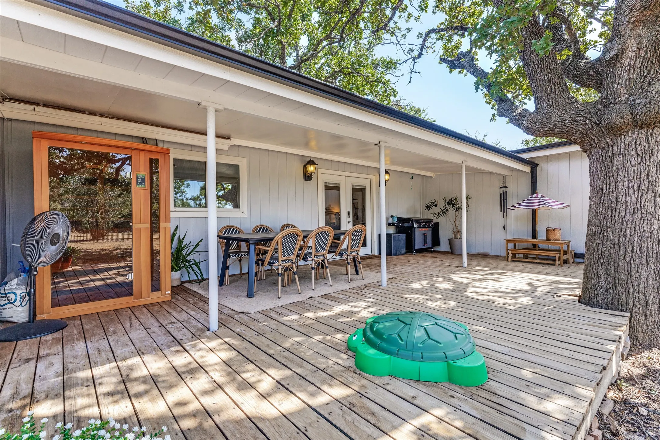 Expansive outdoor deck with a covered patio area, wood siding, and mature trees