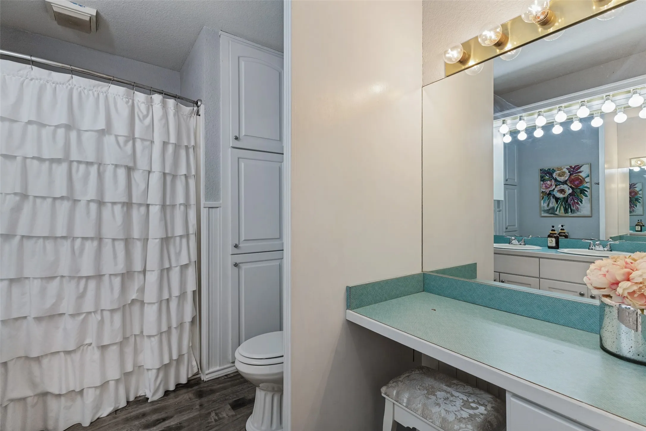 Built-in cabinetry providing vertical storage, wood-finish flooring, and a vanity area with a large wall mirror