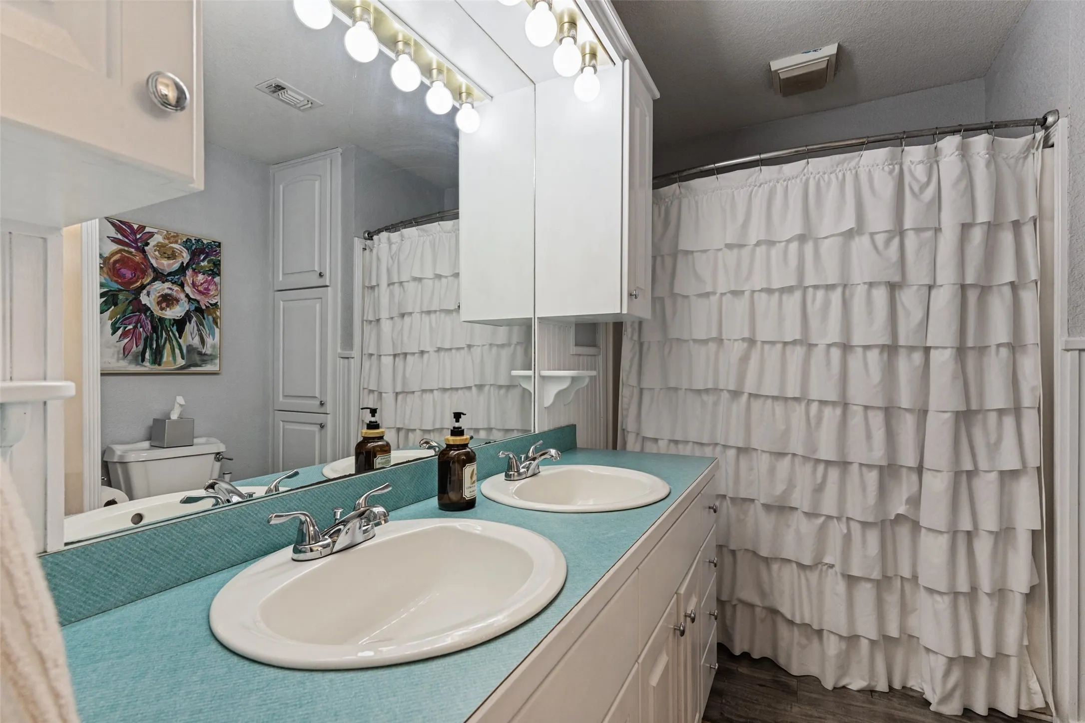 Double vanity with individual sinks, white cabinetry, light fixture with exposed bulbs, full-width mirror, and built-in storage cabinet