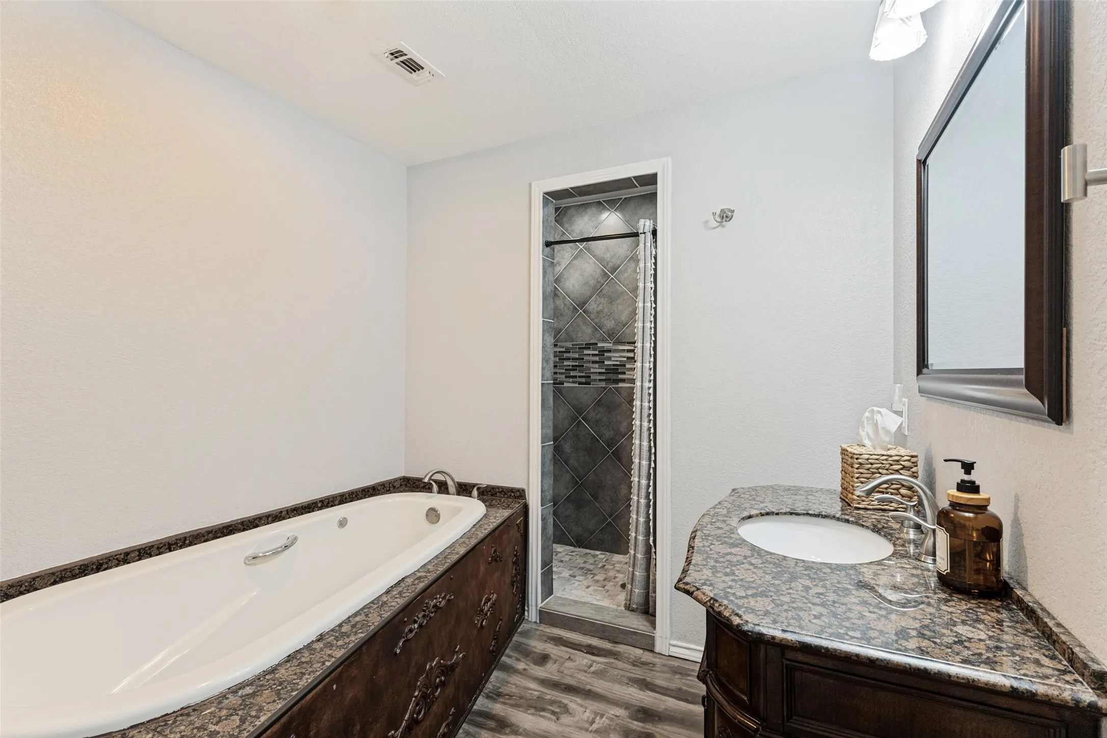 Bathroom featuring an integrated soaking tub, wood-finish flooring, a vanity with a counter-mounted sink, and a separate shower enclosure with tiled walls