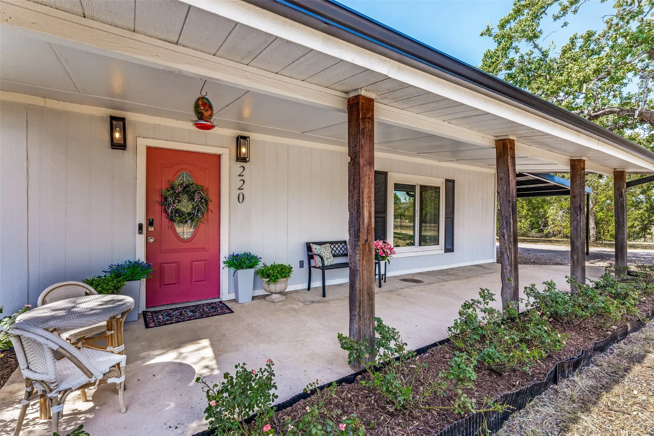 Covered front porch featuring natural wood columns, a red entry door, and exterior wall sconces