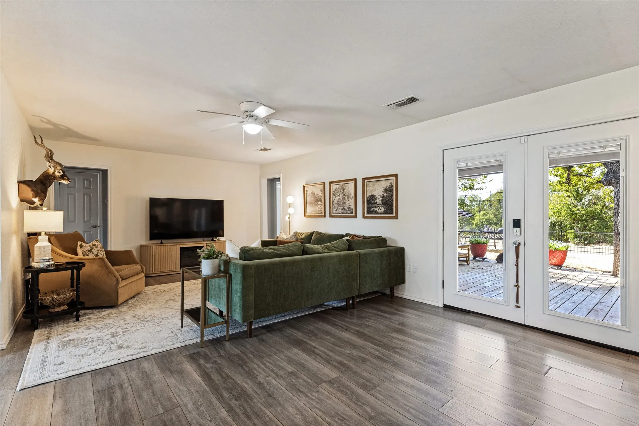 Wood-finish flooring throughout, white walls, ceiling fan with integrated lighting, and double glass-paneled doors opening to an exterior deck