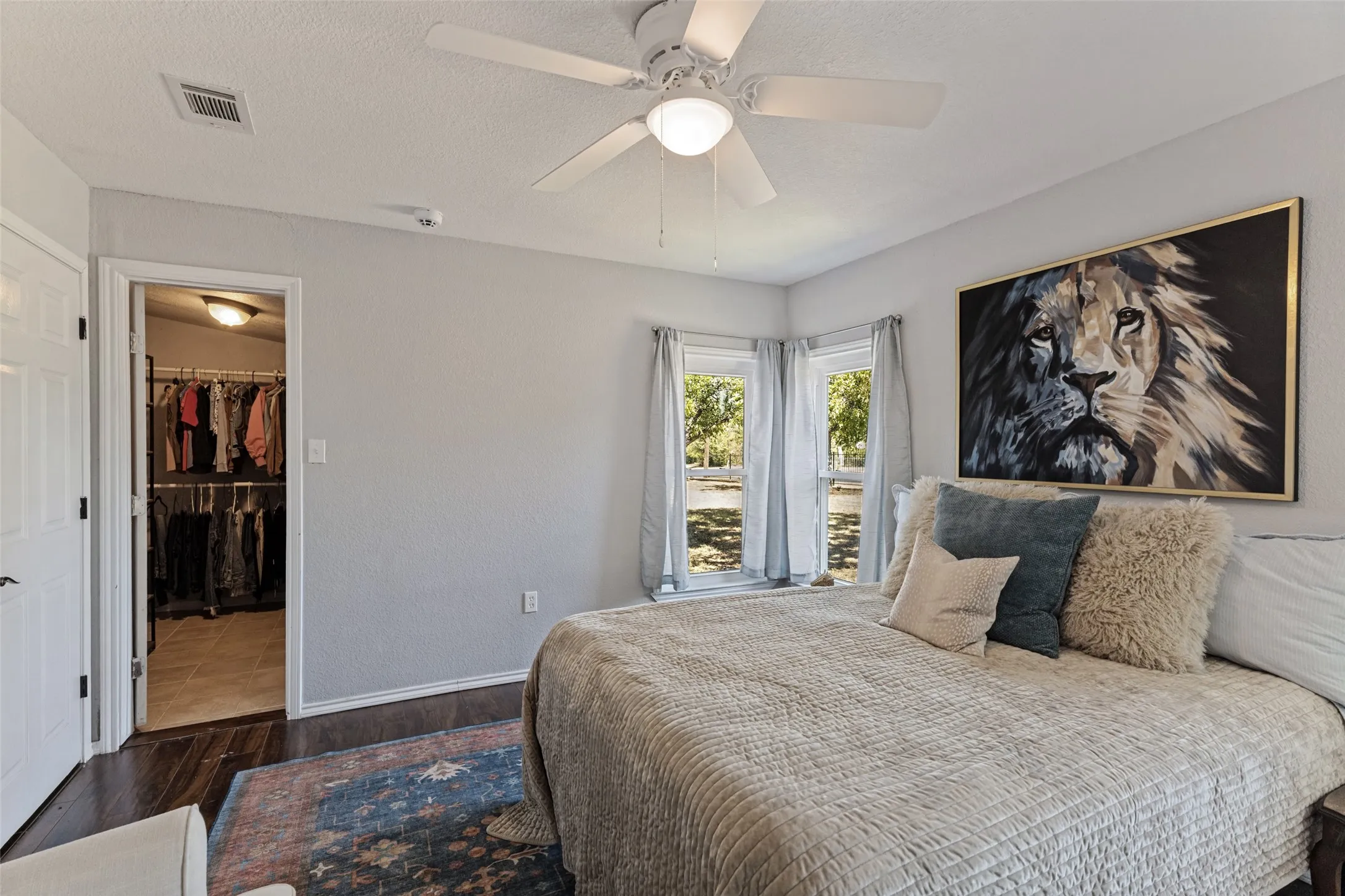 Recessed corner windows, wood-finish flooring, white ceiling fan with integrated lighting, and an open doorway to a walk-in closet with built-in shelving