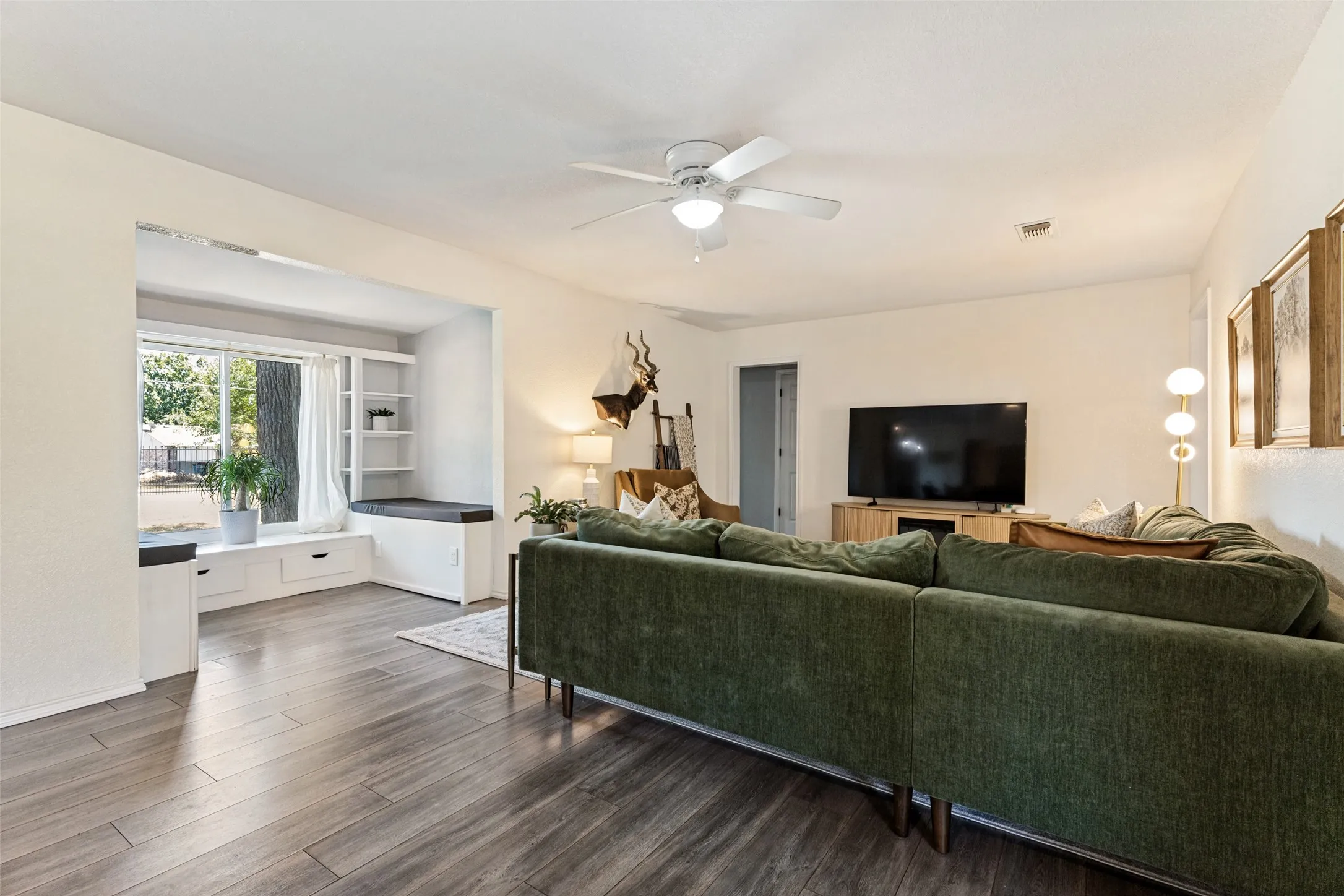Wood-finish flooring throughout, integrated window seating with storage, built-in shelving, and a ceiling fan