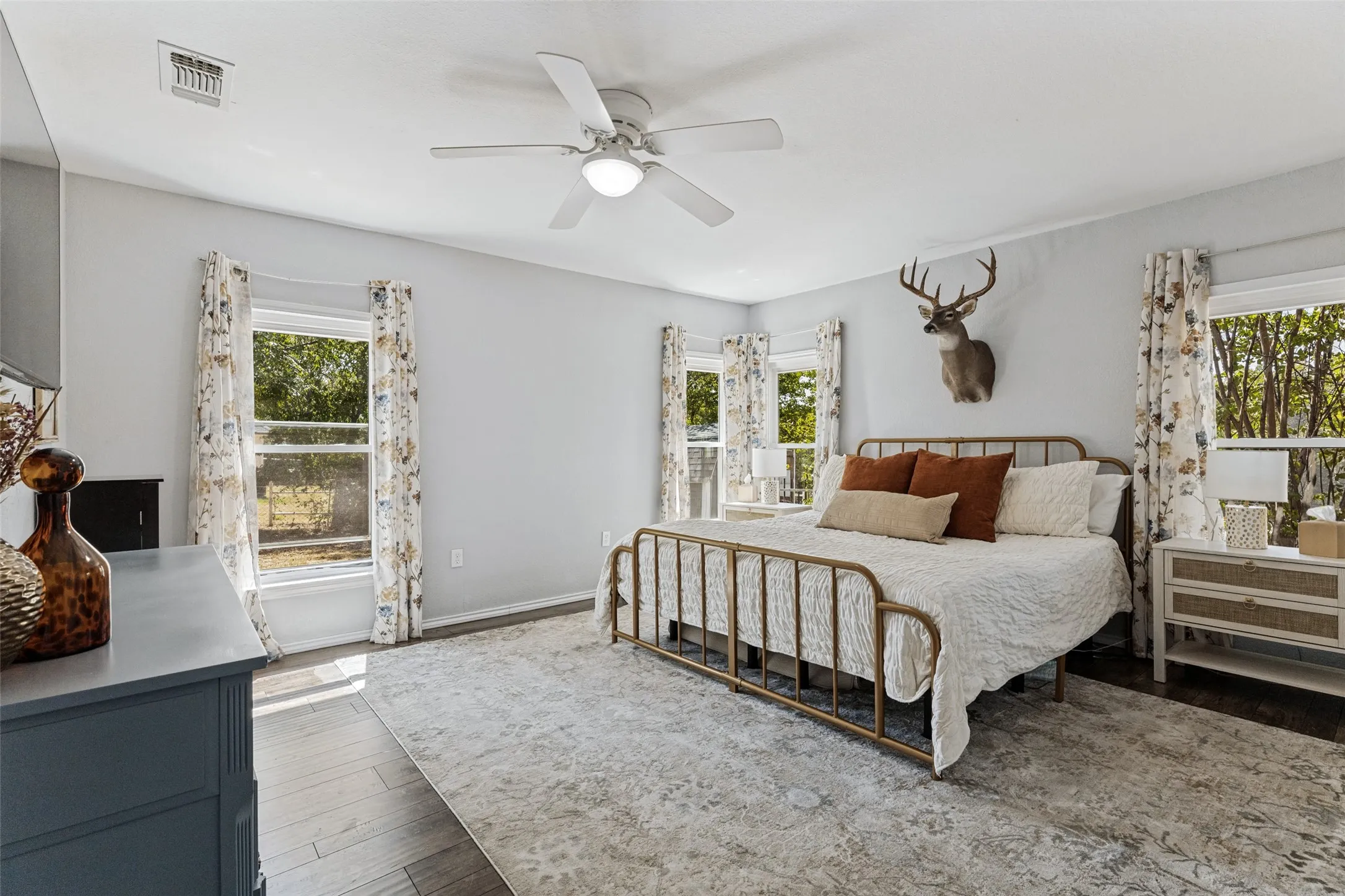 Light gray walls with multiple windows, wood-finish flooring, and a ceiling fan with integrated lighting