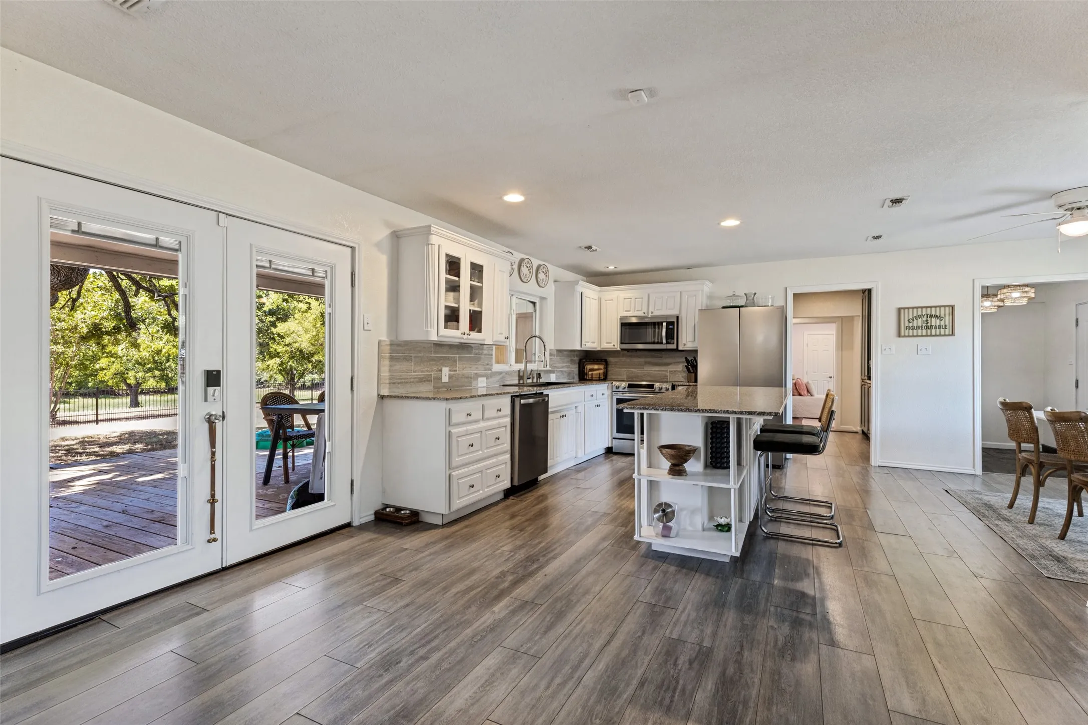 Wood-finish flooring throughout, kitchen with white cabinetry, stainless steel appliances, central island with seating, and French doors opening to an exterior deck