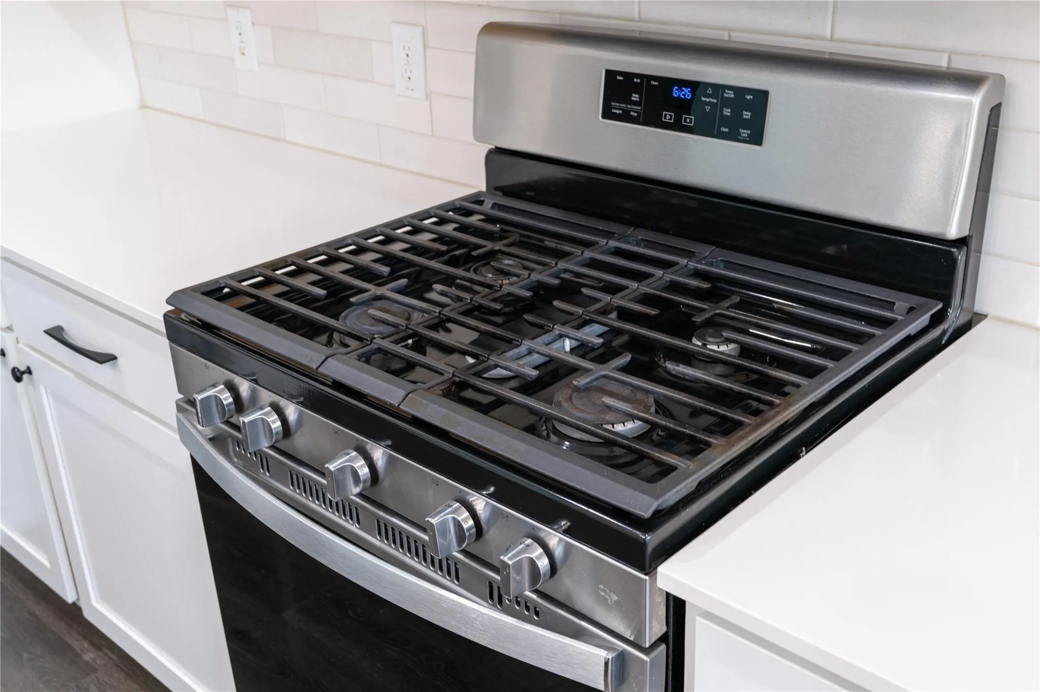 Stainless steel range with gas burners, white countertops, and white subway tile backsplash