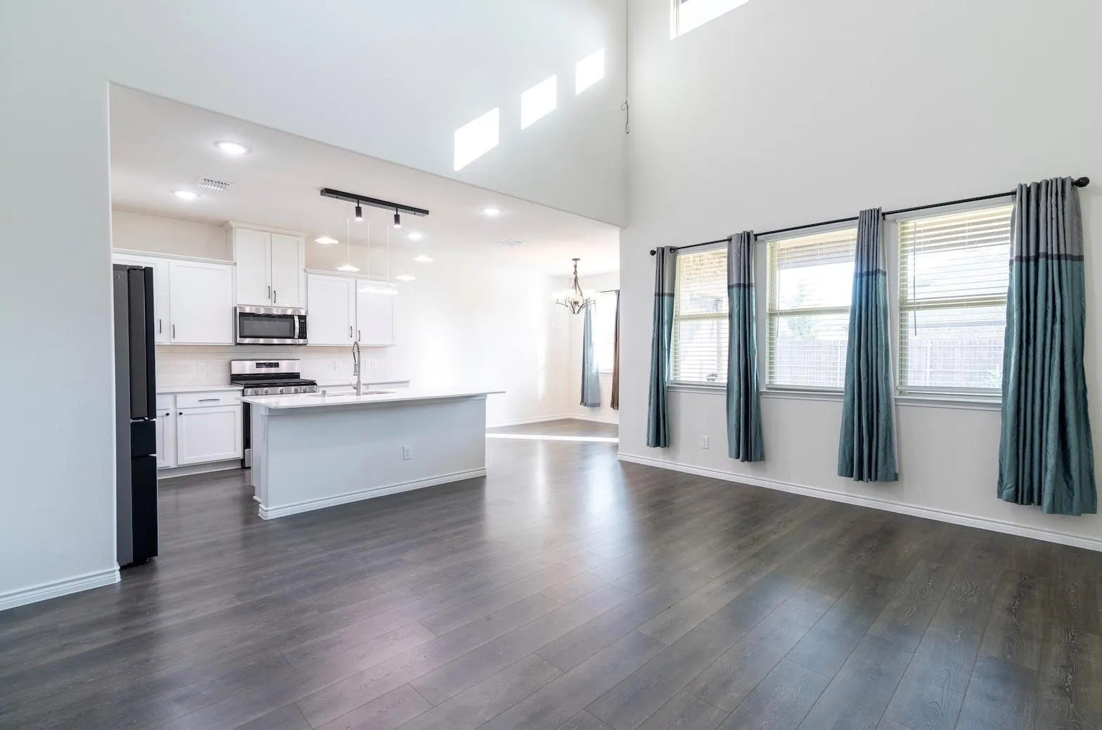 Open-concept design featuring wood-finish flooring, high ceilings, and a kitchen with white cabinetry