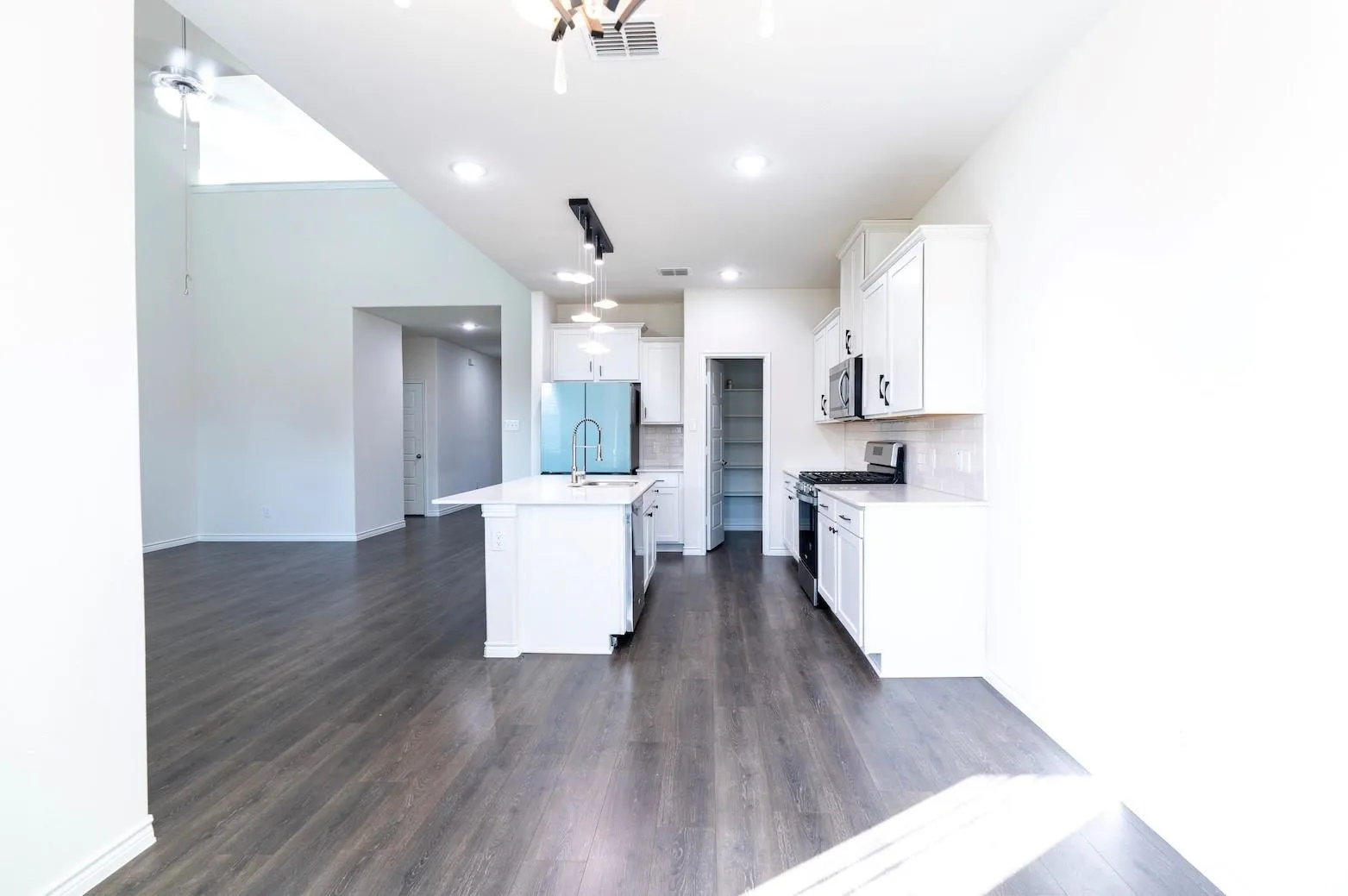 Kitchen featuring an island with a sink, white cabinetry with matte black hardware, and a tile backsplash