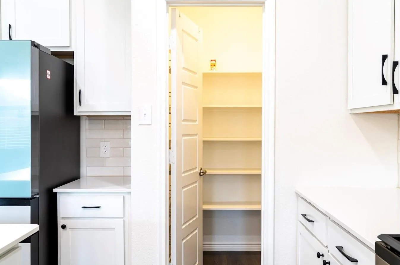 White cabinetry with black hardware, light subway tile backsplash, white countertops, and a walk-in pantry with built-in shelving
